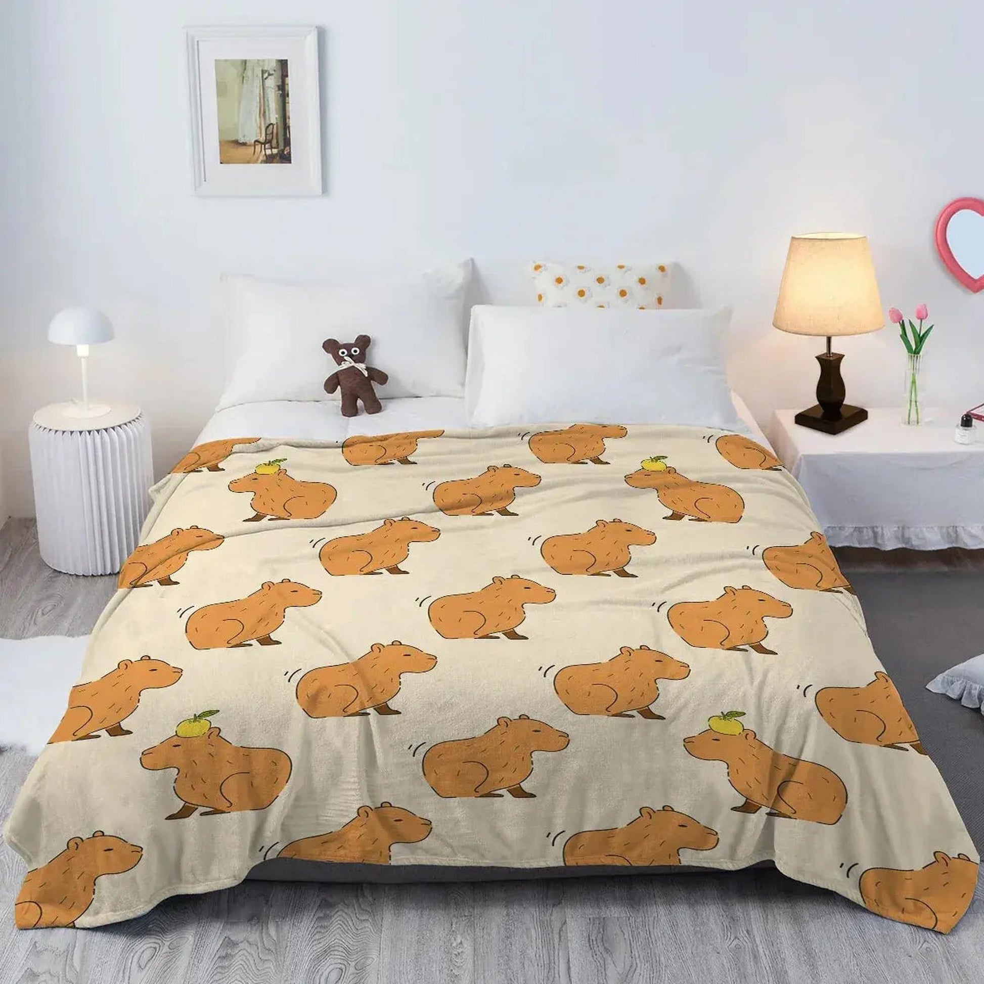 Cream flannel blanket with a playful pattern of brown capybaras, some with a green apple on their head, draped on a bed.