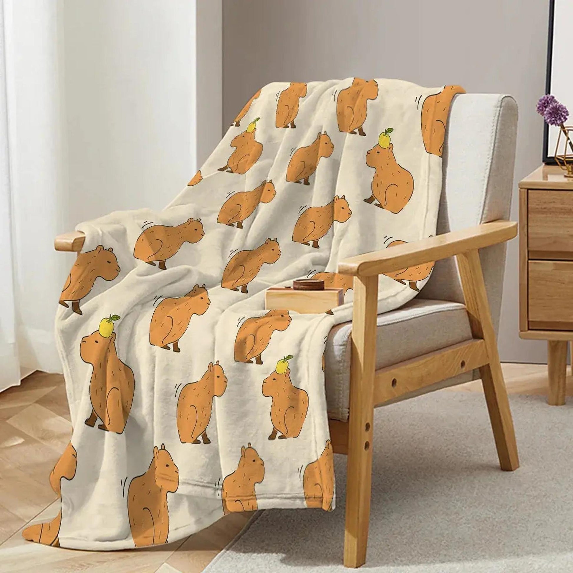Cream flannel blanket with playful brown capybara print, draped over a light wood armchair.