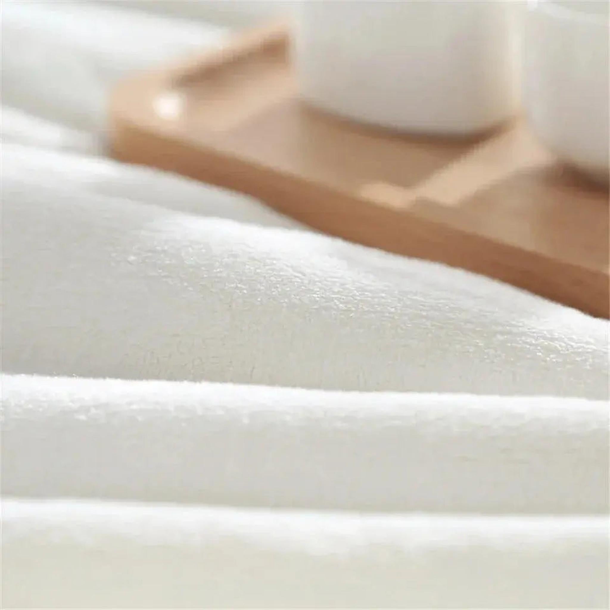 Close-up of a soft, plush white flannel blanket with a blurred wooden tray in the background.