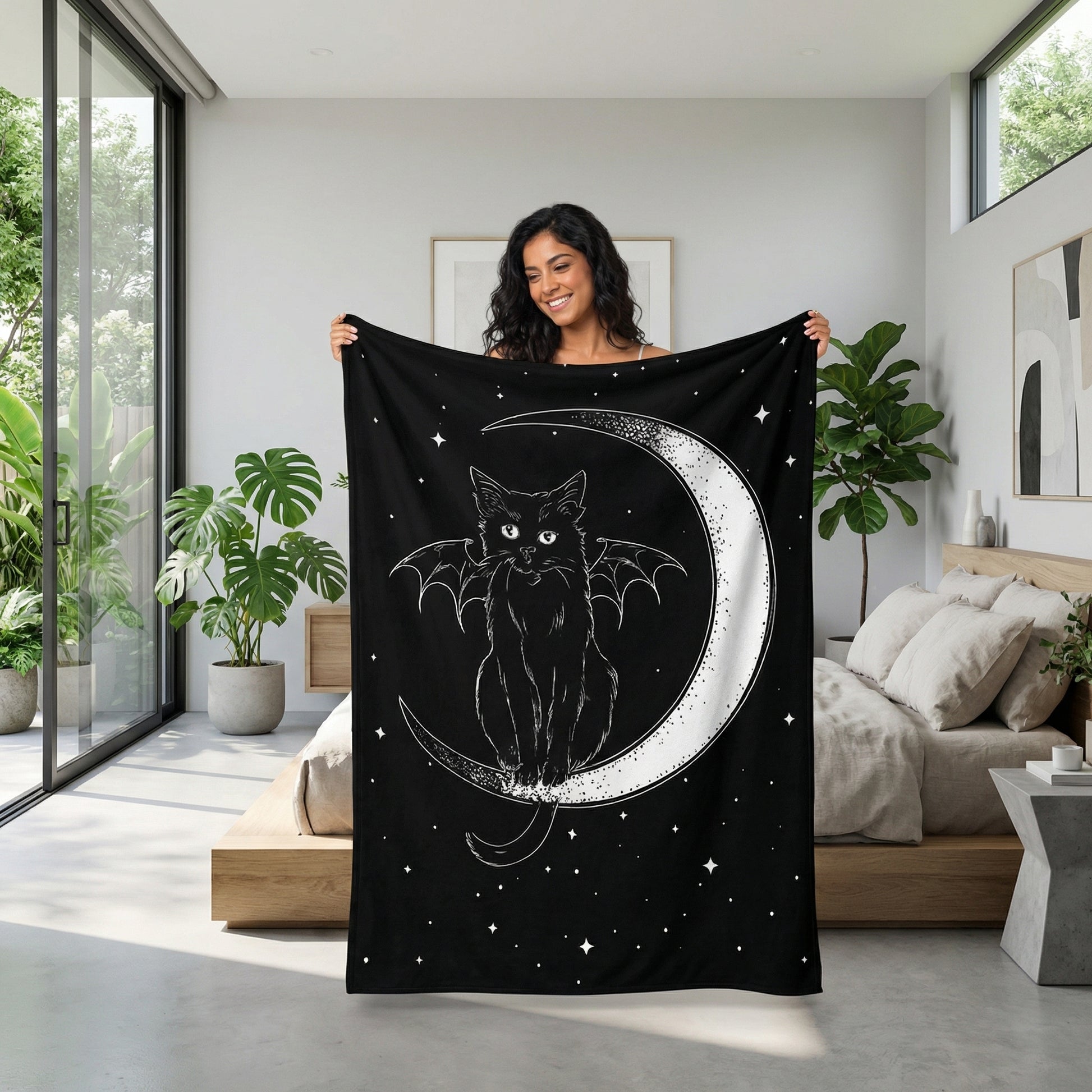 Woman holding a black flannel throw blanket with a white cat with bat wings sitting on a crescent moon design.