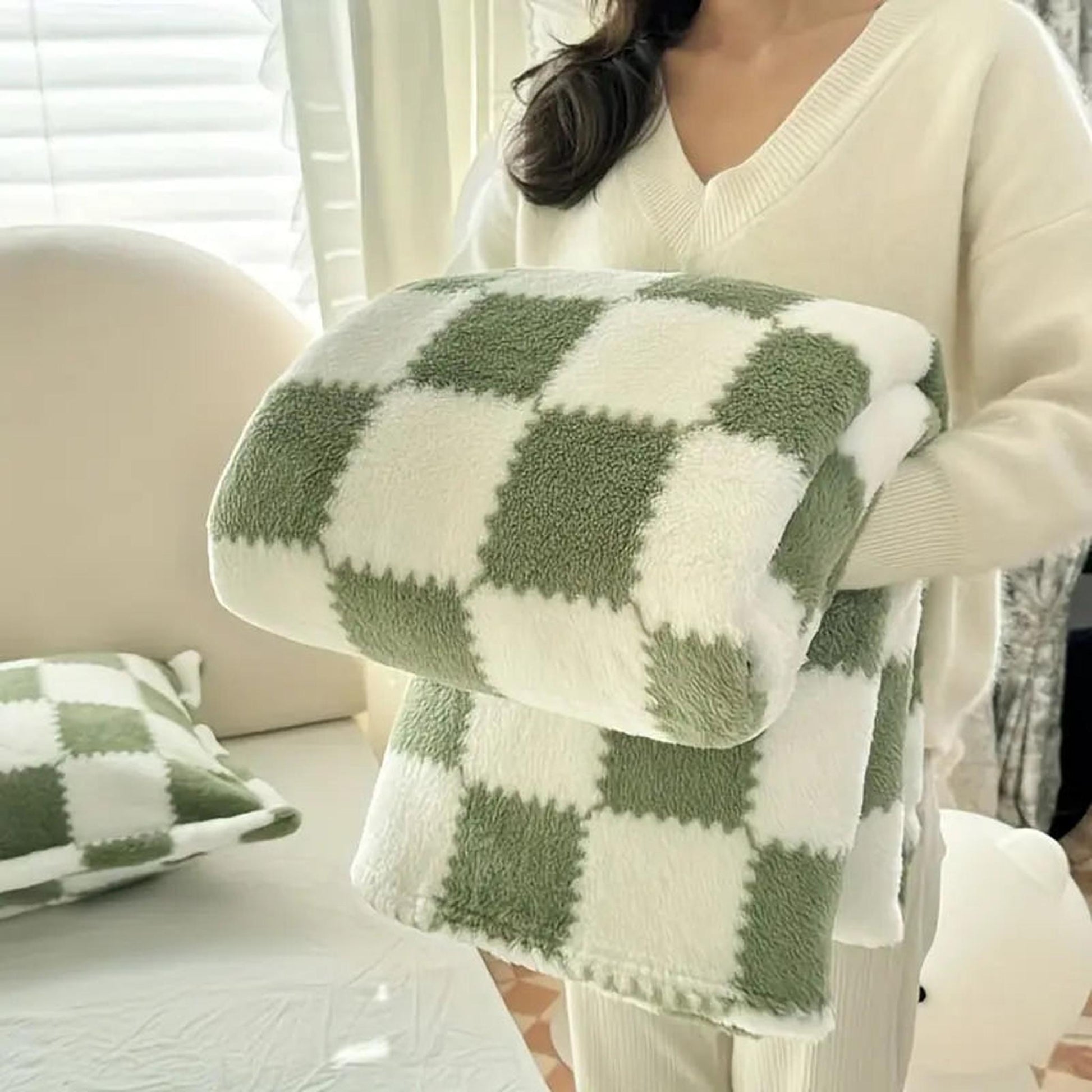 Soft green and white checkered flannel fleece blanket held by a person, with a matching pillow nearby.