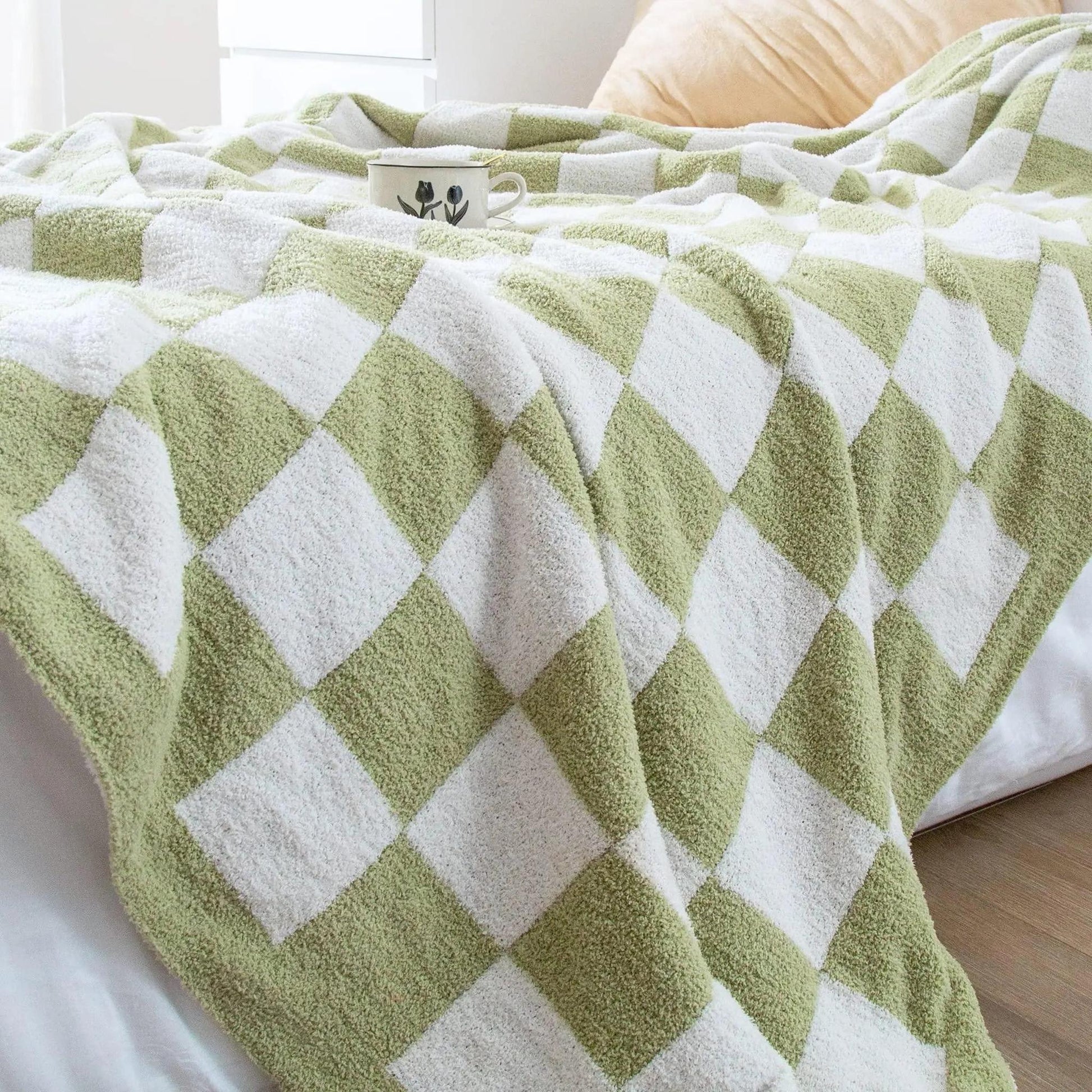 Soft green and white checkered flannel fleece blanket draped on a bed with a cup.