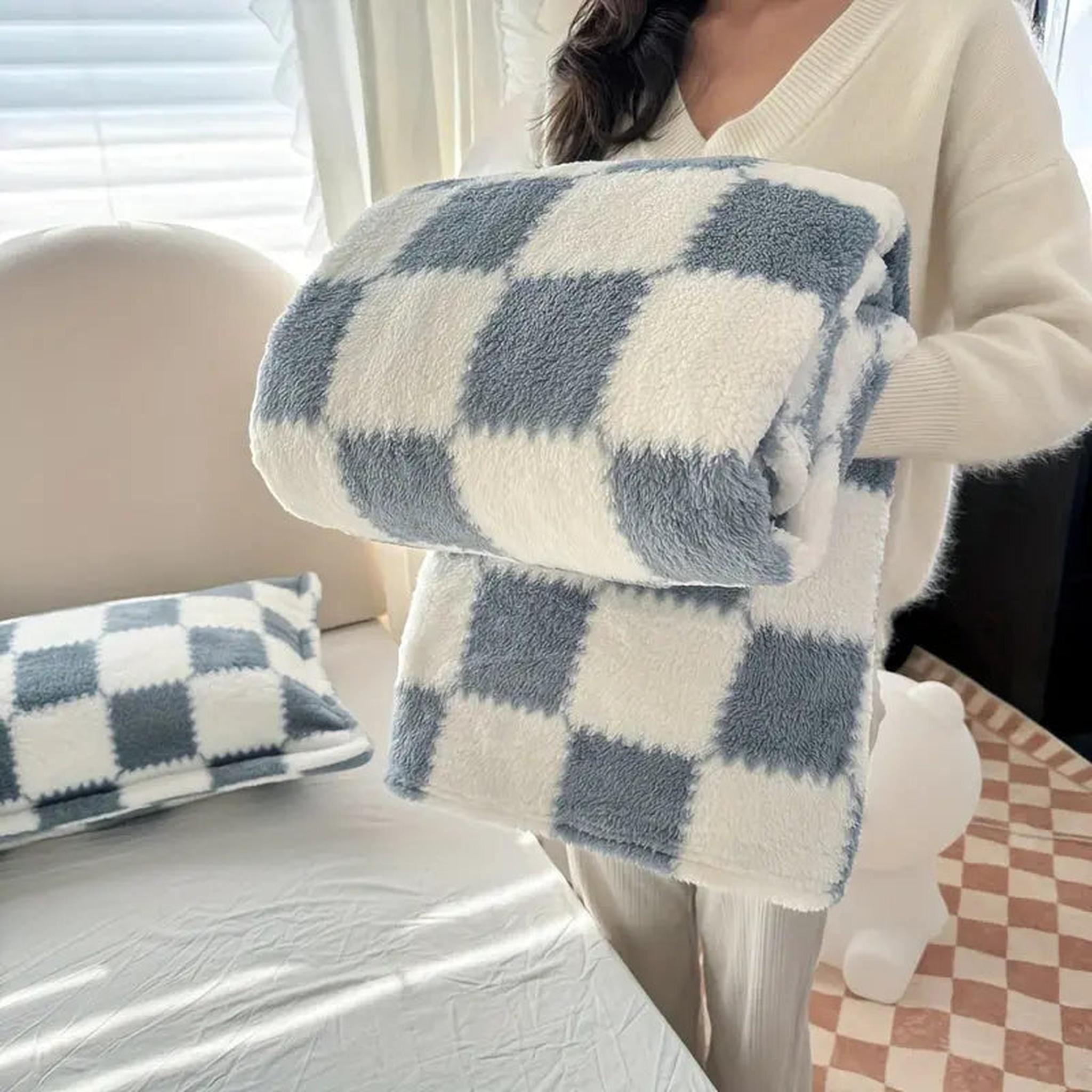 Soft blue and white checkered flannel fleece blanket held by a person, with a matching pillow nearby.