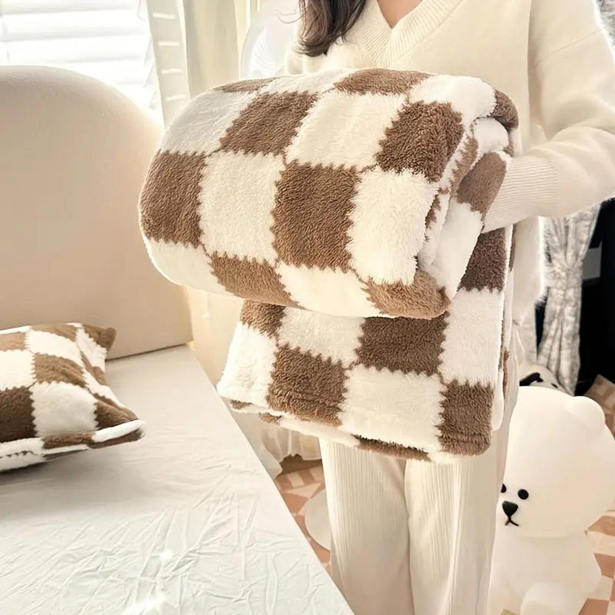 Person holding a folded brown and white checkered flannel fleece blanket with a matching pillow on a bed.