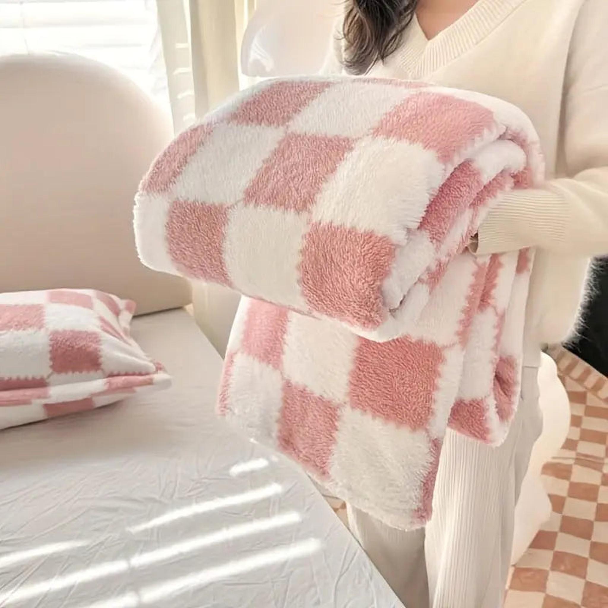 Soft pink and white checkered flannel fleece blanket held by a person, with a matching pillow on a bed.