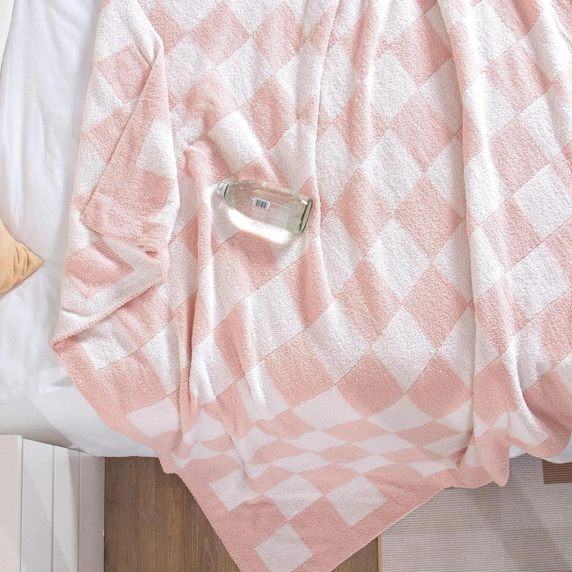 Pink and white checkered flannel fleece blanket draped on a bed, with a glass bottle resting on it.