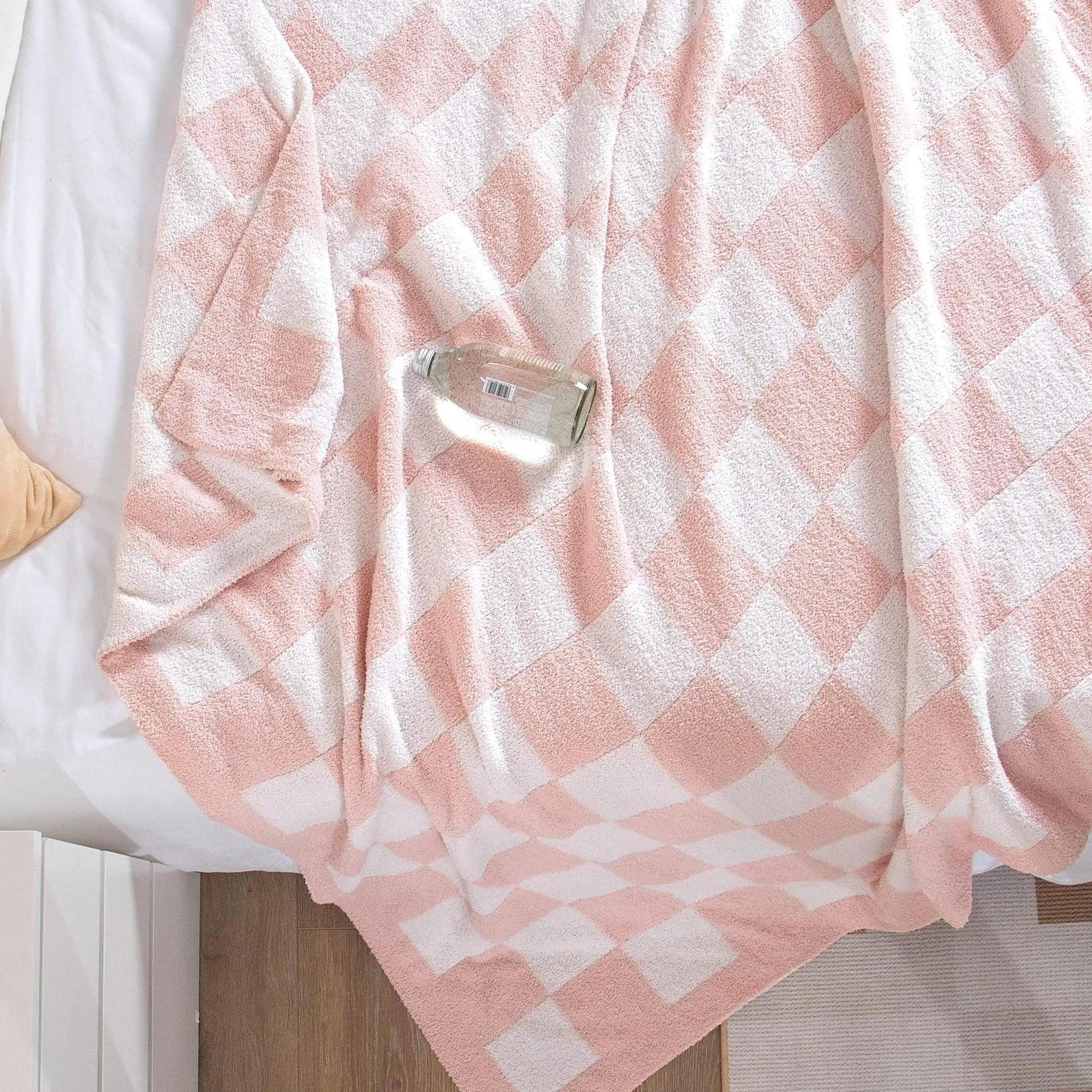 Pink and white checkered flannel fleece blanket draped on a bed, with a glass bottle resting on it.