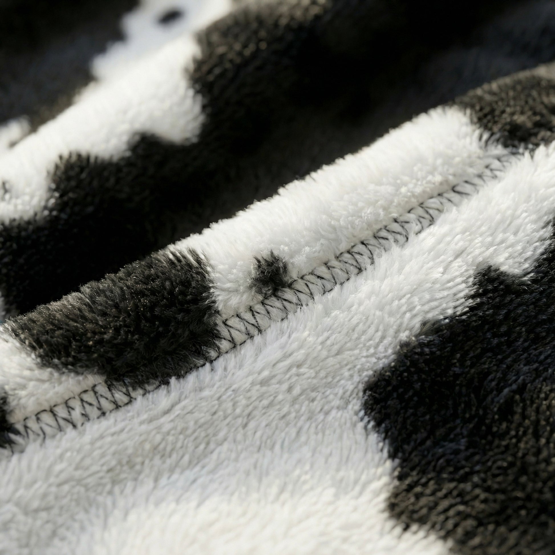 Close-up of a soft, black and white cheetah print flannel fleece blanket with visible stitching.