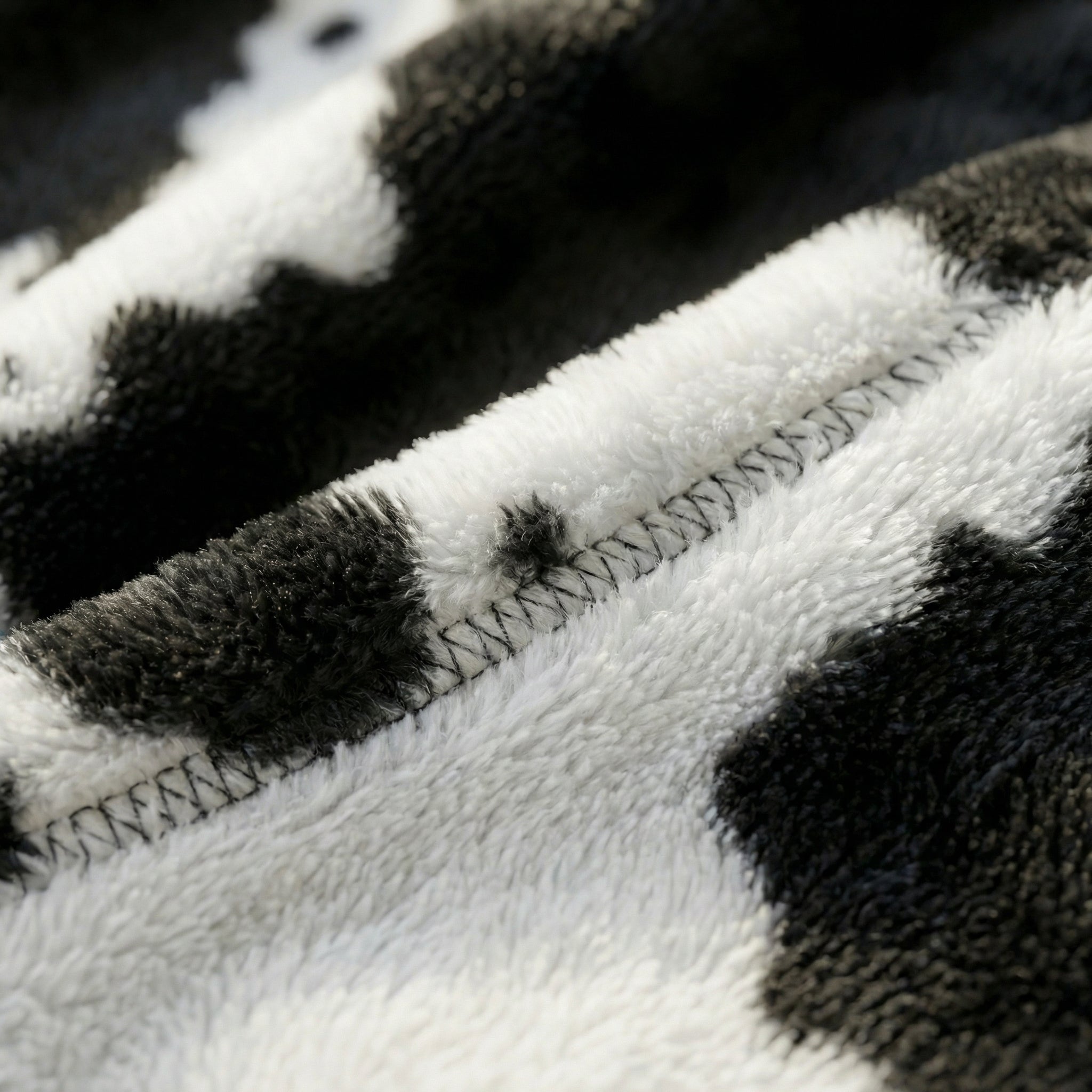 Close-up of a soft, black and white cheetah print flannel fleece blanket with visible stitching.