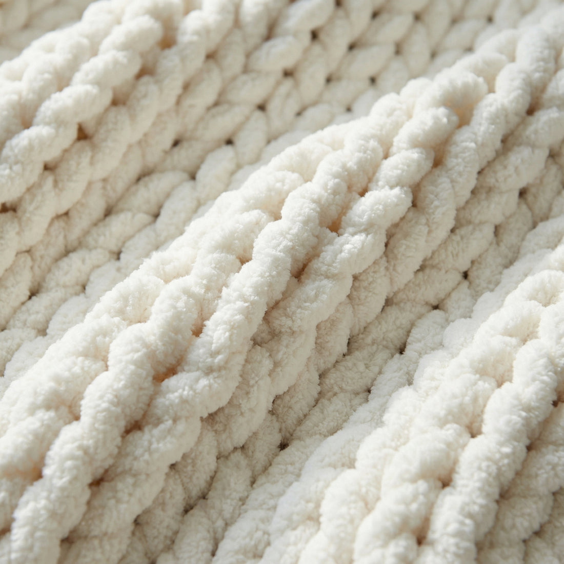 Woman wrapped in a cozy, chunky knit white throw blanket on a light gray sofa, reading a book.