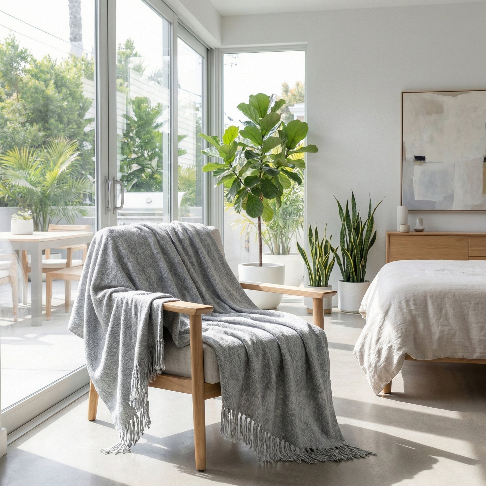 Light gray chenille throw blanket with fringes draped over a modern wooden armchair in a bright room.