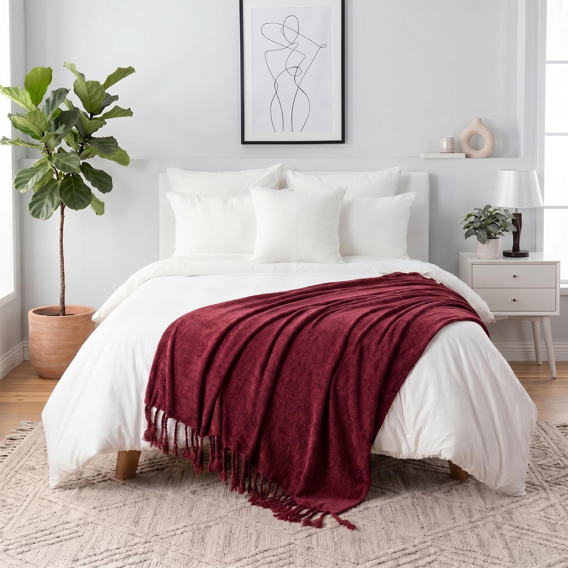 Red chenille throw blanket with fringe tassels draped over a white bed in a modern bedroom.