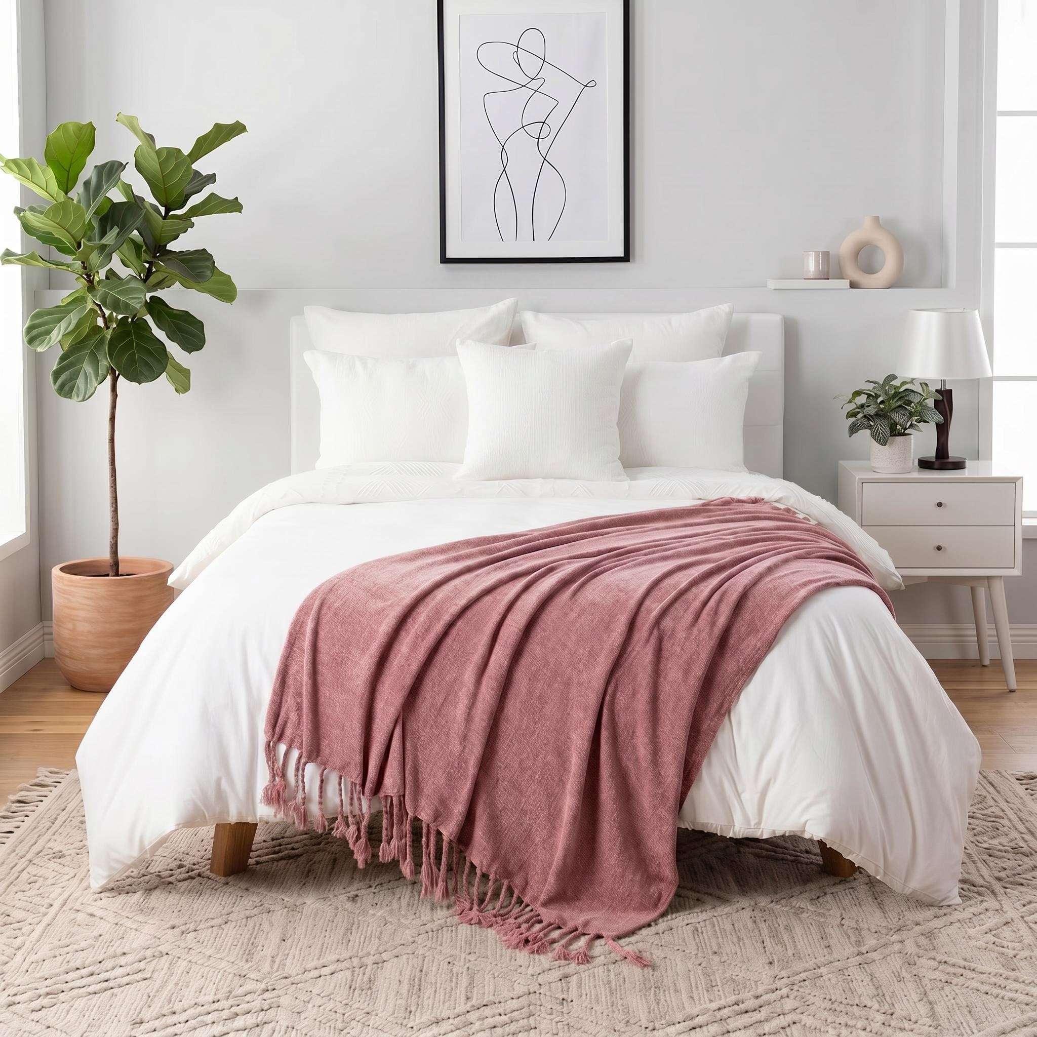 Pink chenille throw blanket with fringe tassels draped over a white bed in a modern bedroom.
