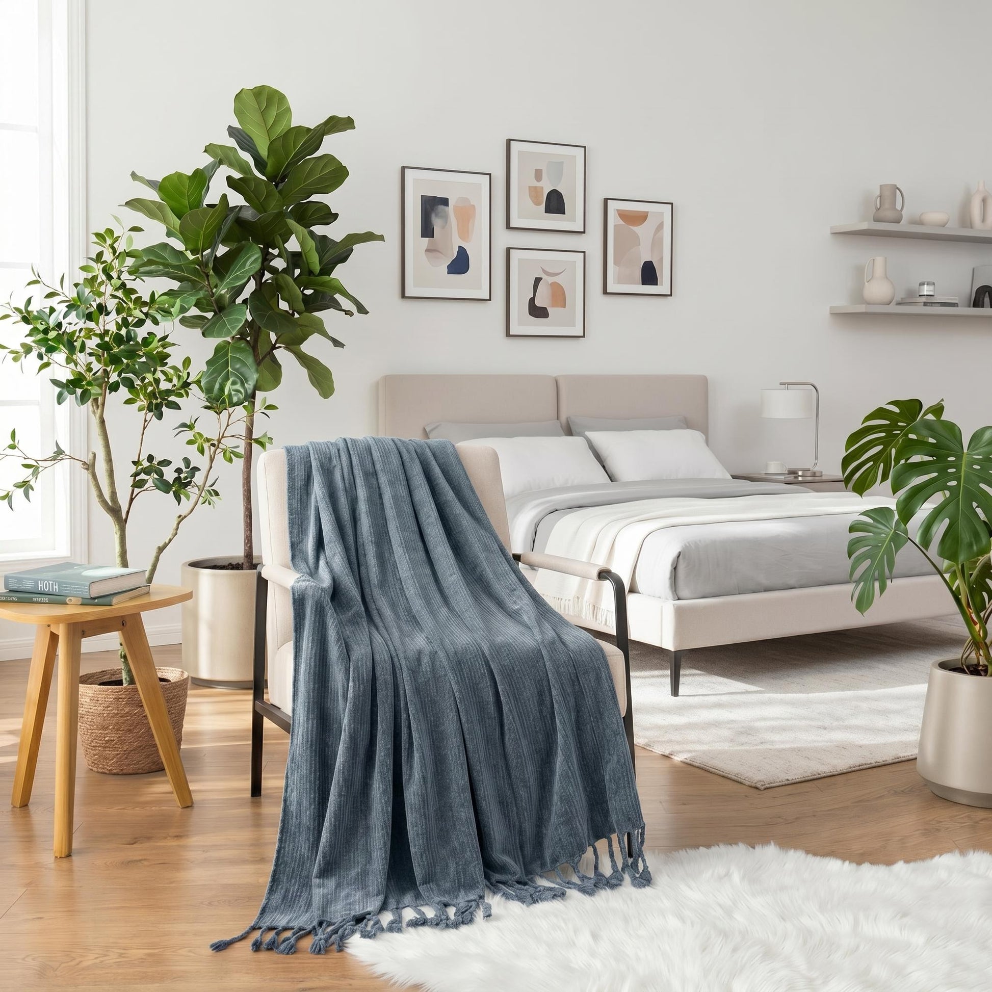 Blue chenille throw blanket with fringe tassels draped over a cream armchair in a modern bedroom.