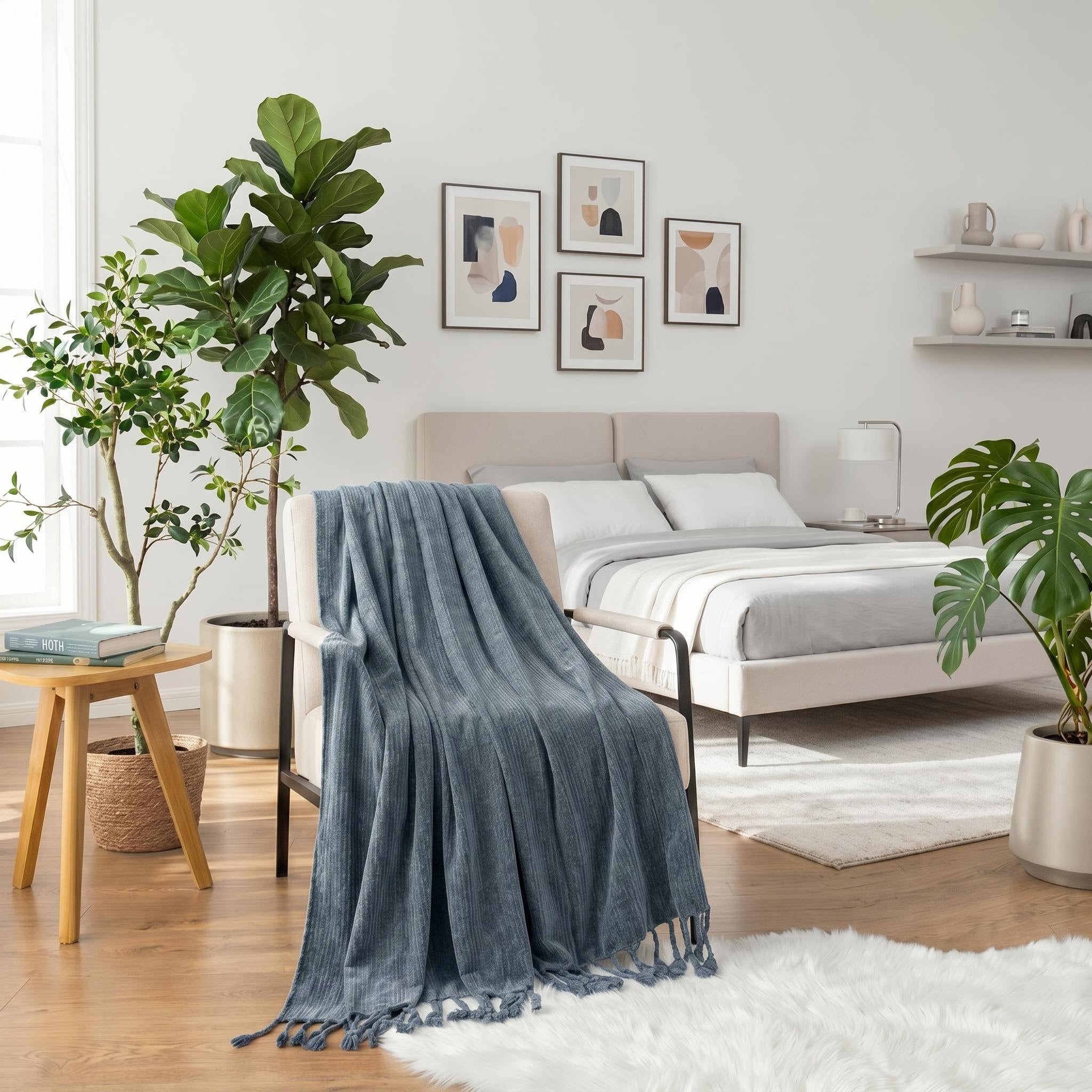 Blue chenille throw blanket with fringe tassels draped over a cream armchair in a modern bedroom.
