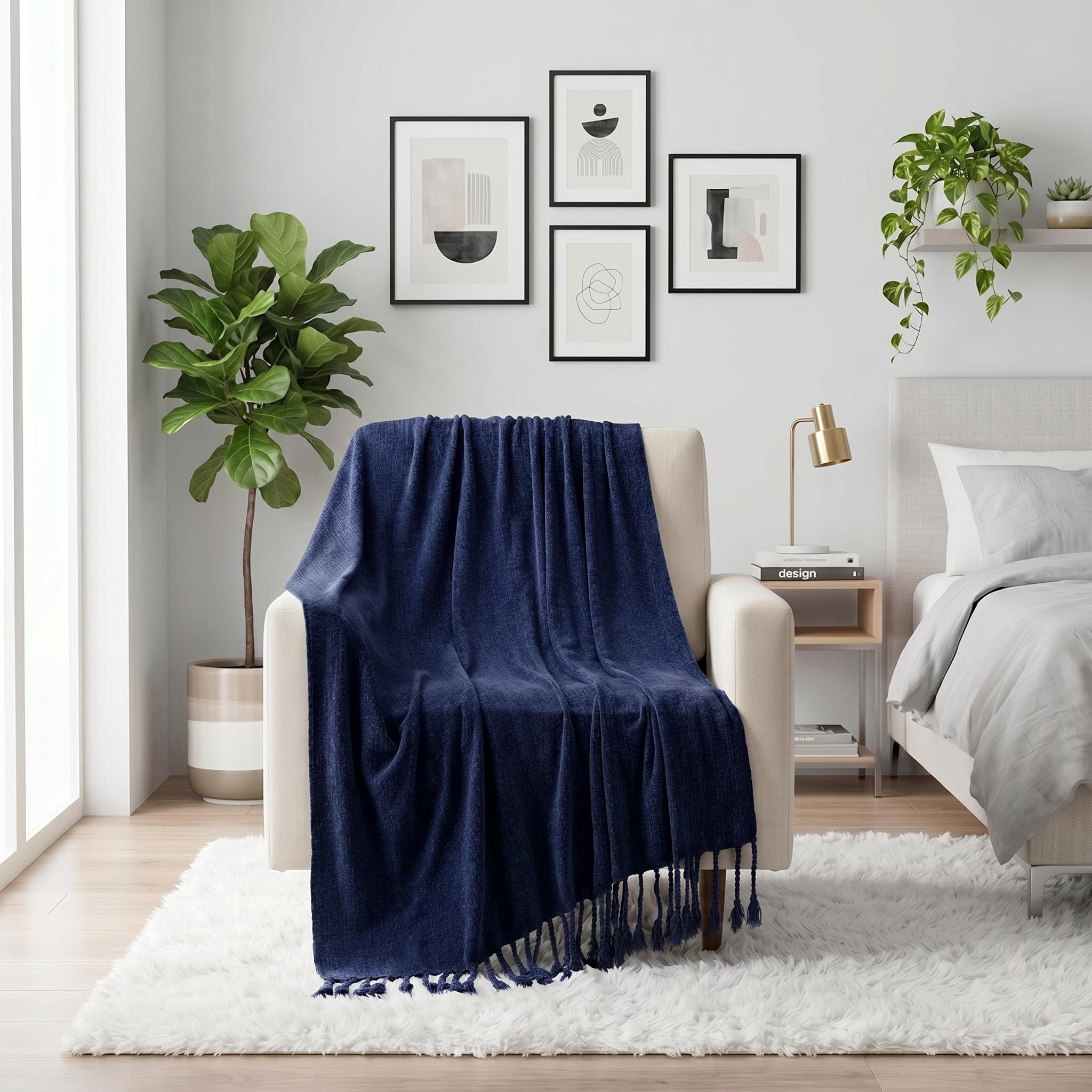 Navy blue chenille throw blanket with fringe tassels draped over a cream armchair in a modern bedroom.
