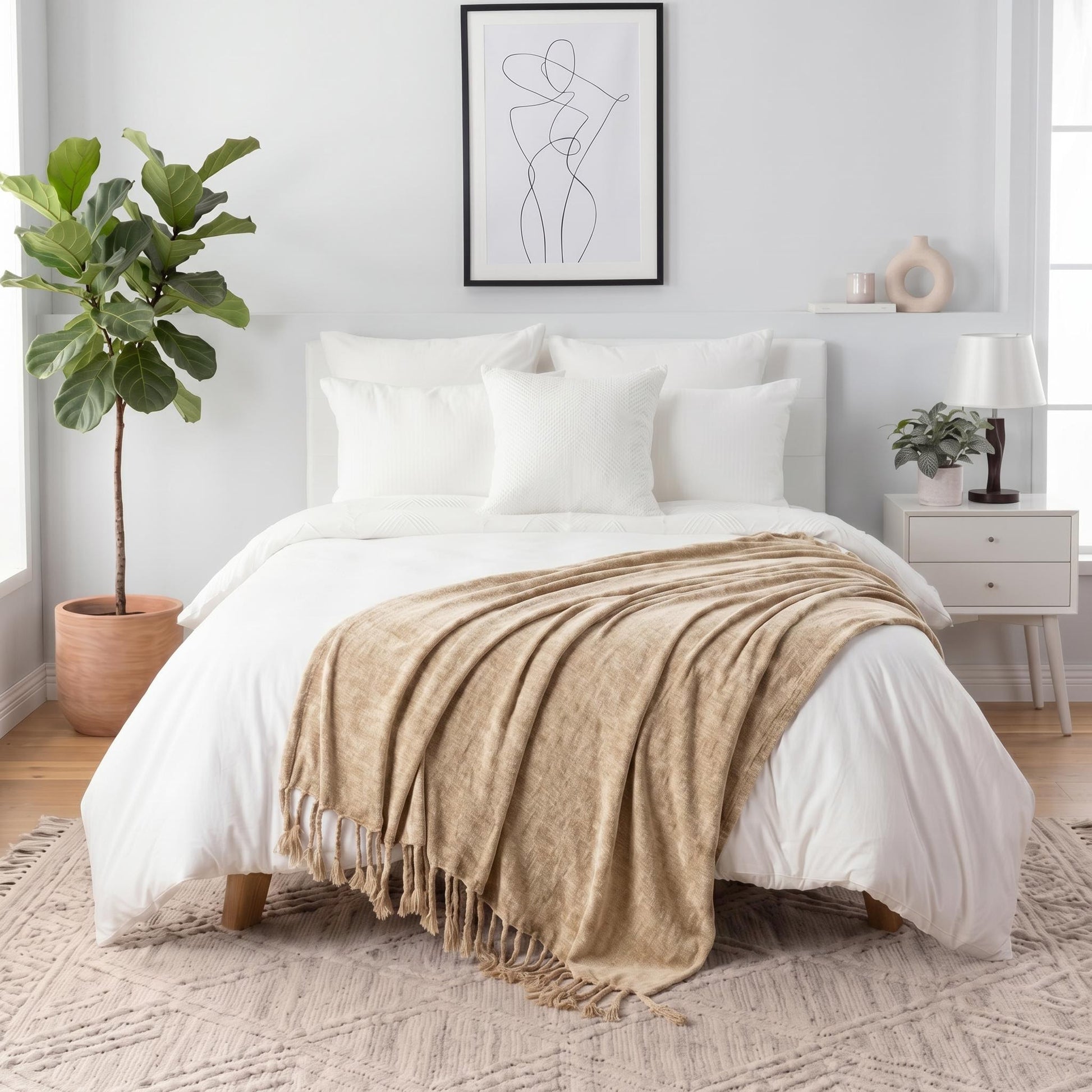 Tan chenille throw blanket with fringe tassels draped over a white bed in a bright bedroom.