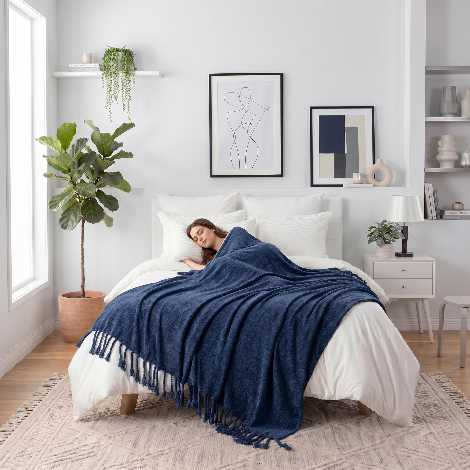 Woman sleeping peacefully under a soft, navy blue chenille throw blanket with fringe tassels on a white bed.