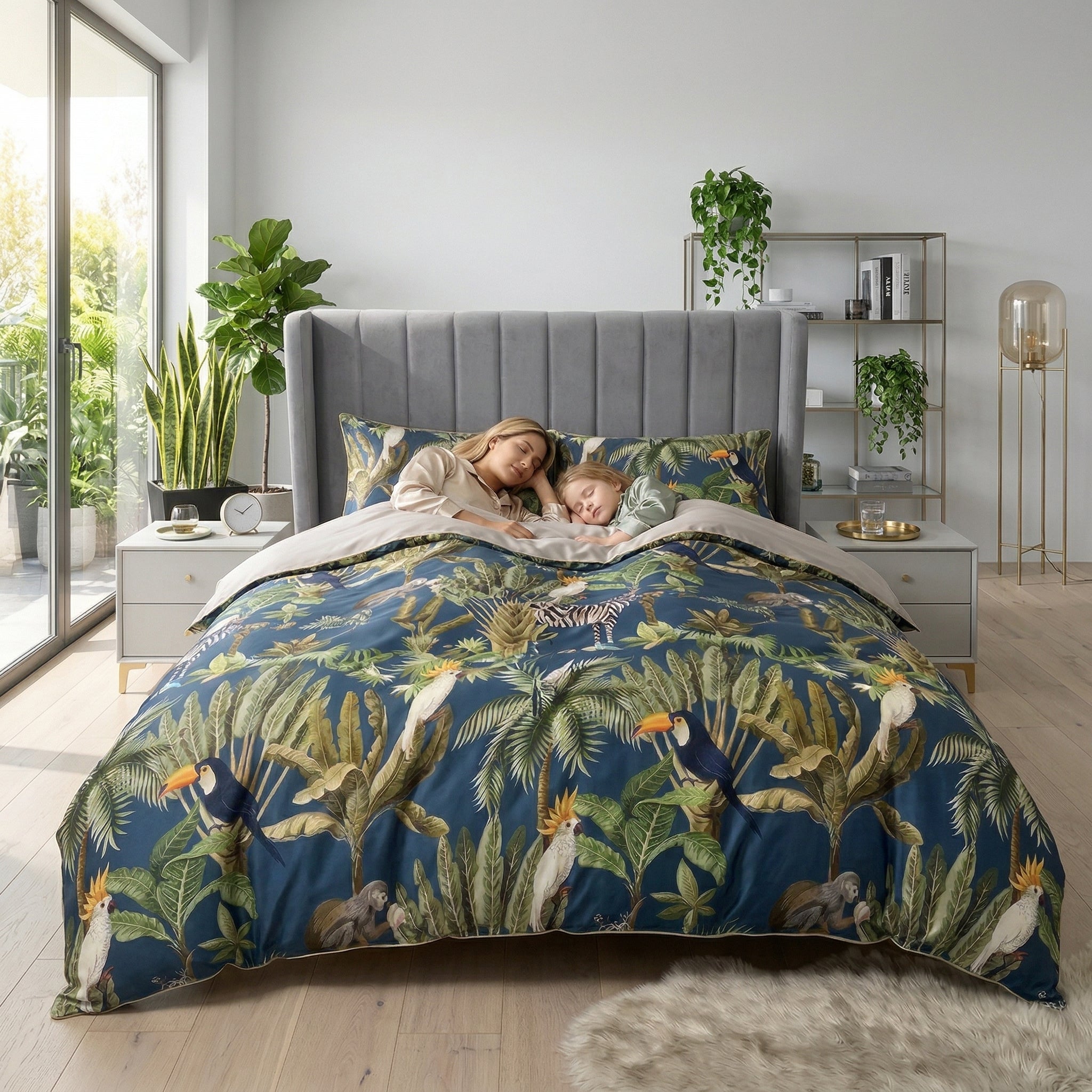 King size bed with blue tropical duvet cover set, featuring toucans, monkeys, and palm leaves, with a woman and child sleeping.