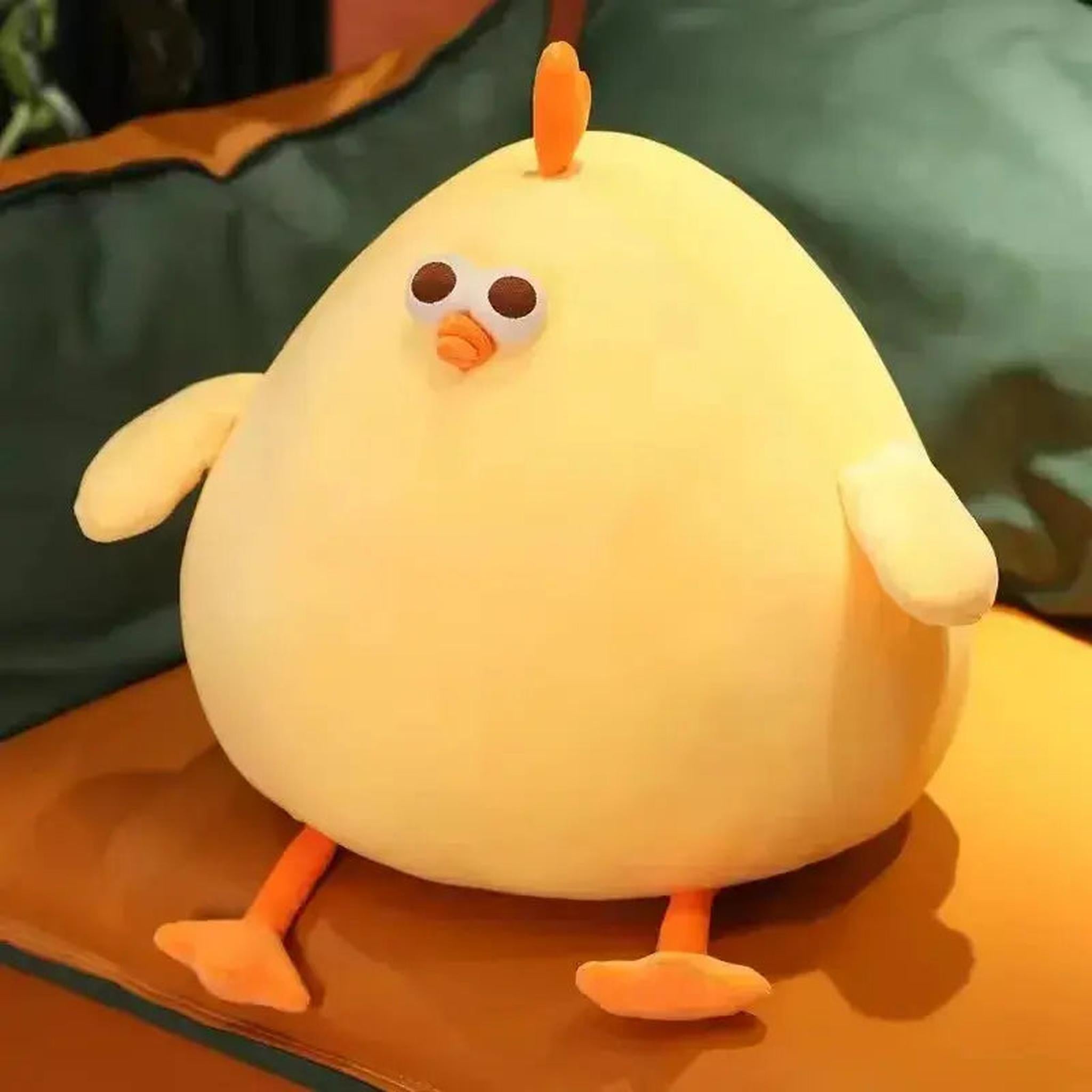 Bright yellow, round plush chubby chicken pillow with small orange feet, beak, and comb, sitting on a brown cushion.