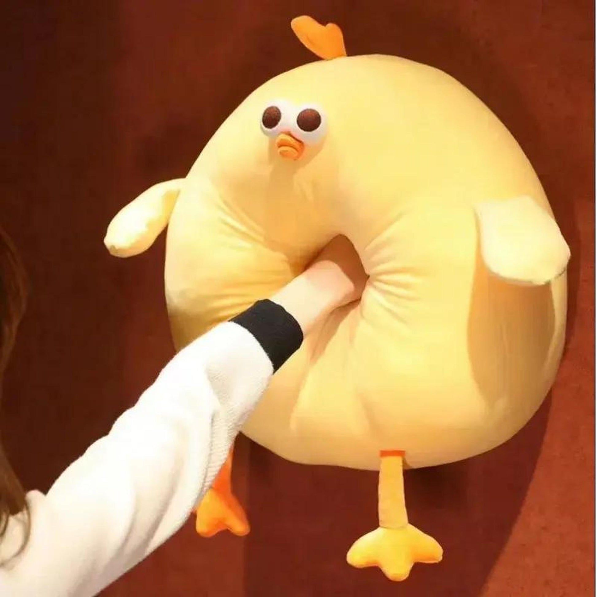 Bright yellow round chubby chicken plush pillow with a hand playfully pushed through its center.