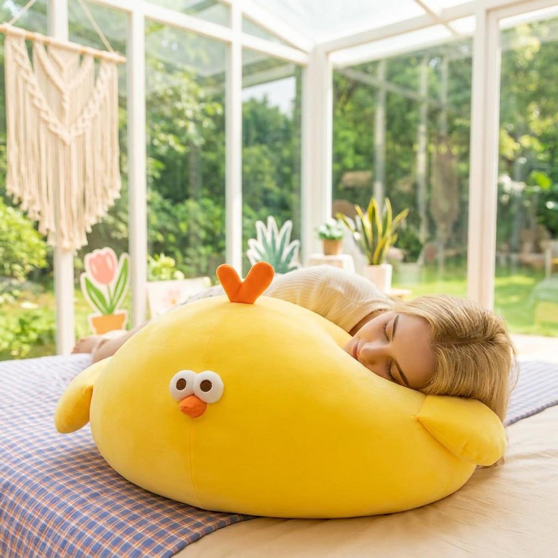 Bright yellow round plush chicken pillow with orange beak and crest, used as a comfortable cushion by a sleeping person.