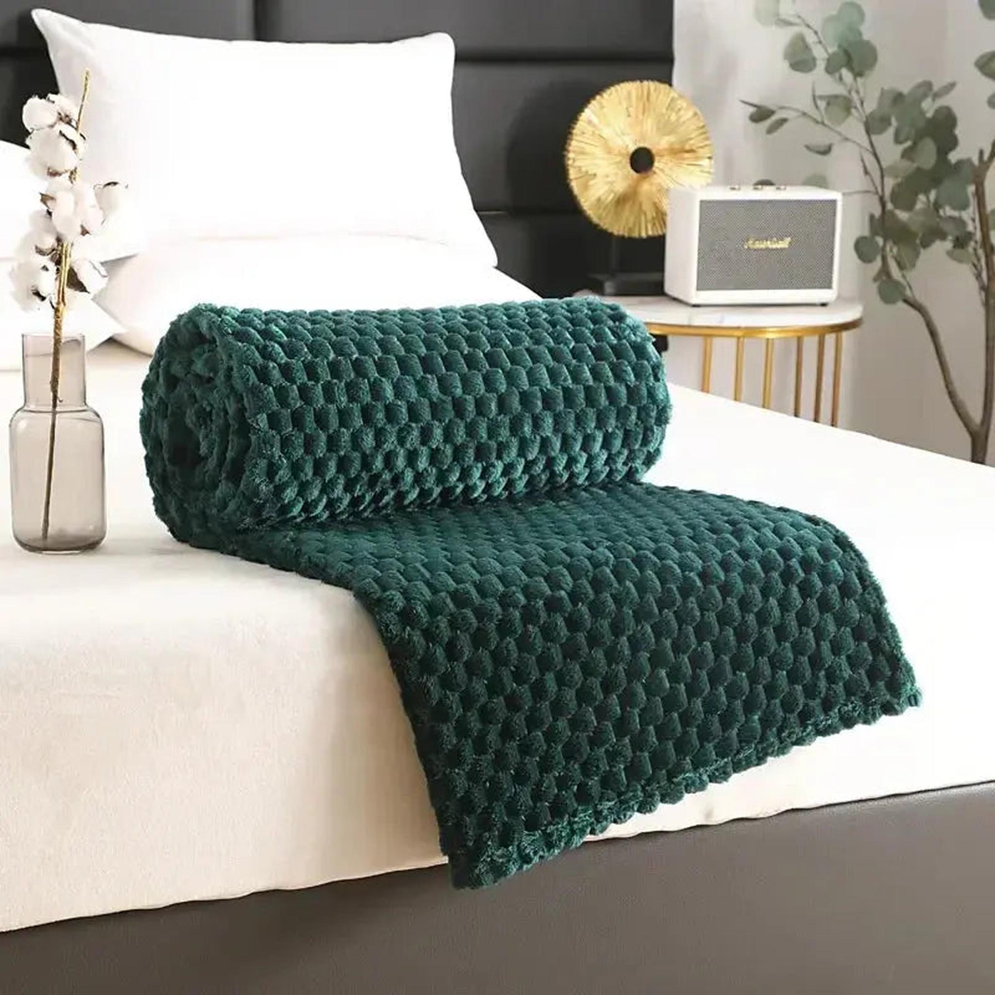 Rolled dark green jacquard fleece blanket with a 3D cloud pattern on a white bed.