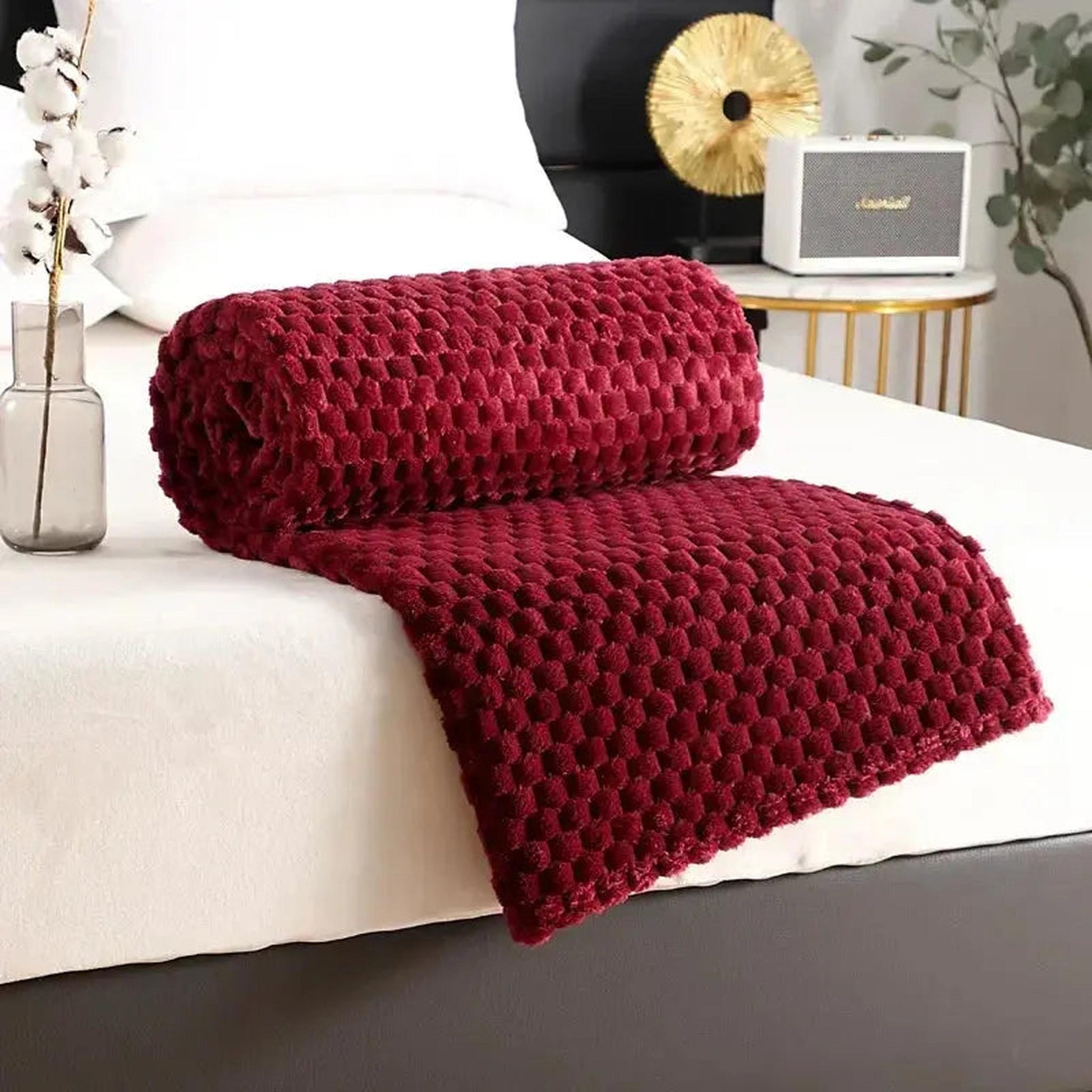 Rolled deep red jacquard fleece blanket with a 3D cloud pattern on a white bed.