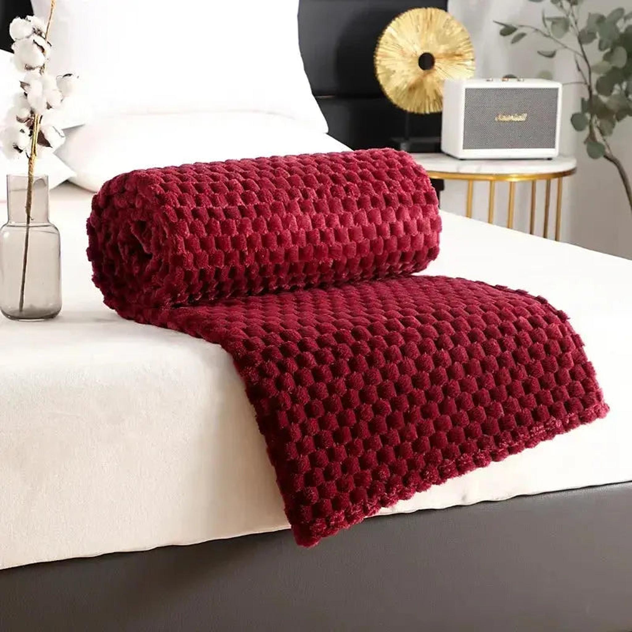 Rolled deep red jacquard fleece blanket with a 3D cloud pattern on a white bed.