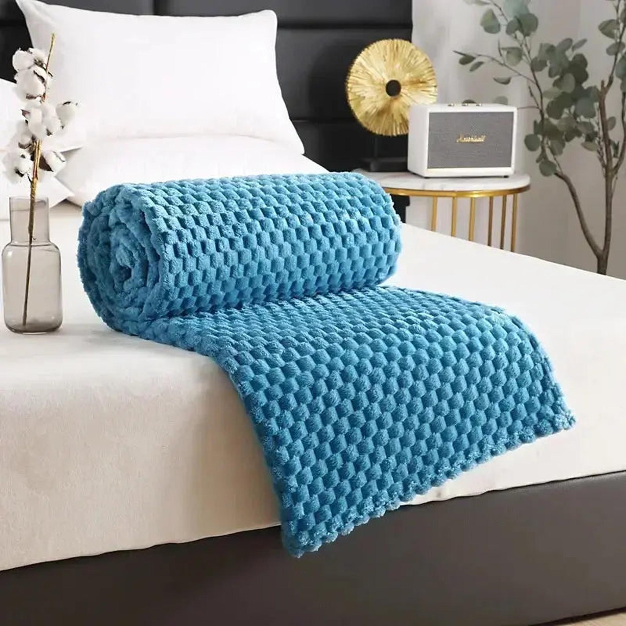 Rolled blue silky flannel fleece blanket with a 3D cloud jacquard pattern on a bed.
