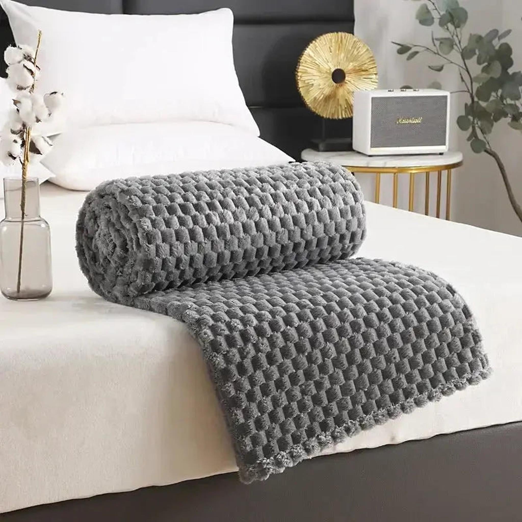 Rolled gray silky flannel fleece blanket with a 3D cloud jacquard pattern on a white bed.
