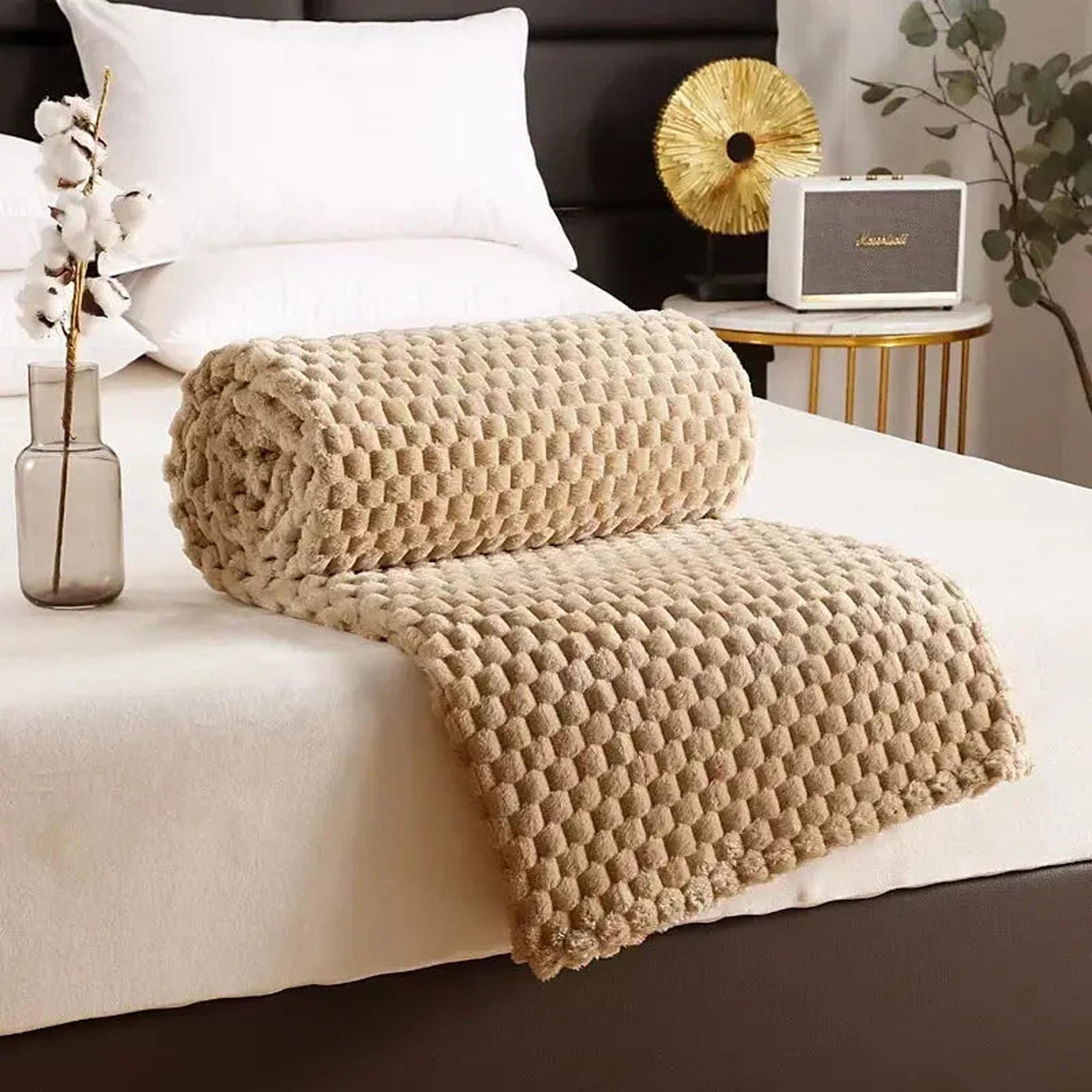 Rolled beige silky flannel fleece blanket with a 3D cloud jacquard pattern on a bed.