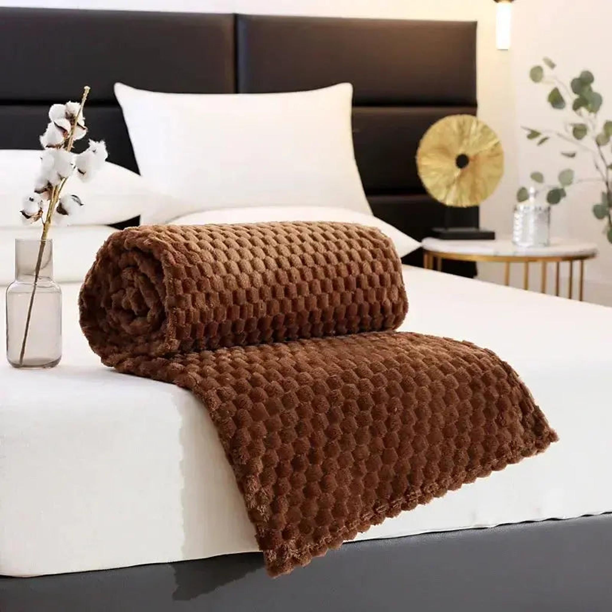 Brown jacquard fleece blanket with 3D cloud pattern, rolled on a white bed.