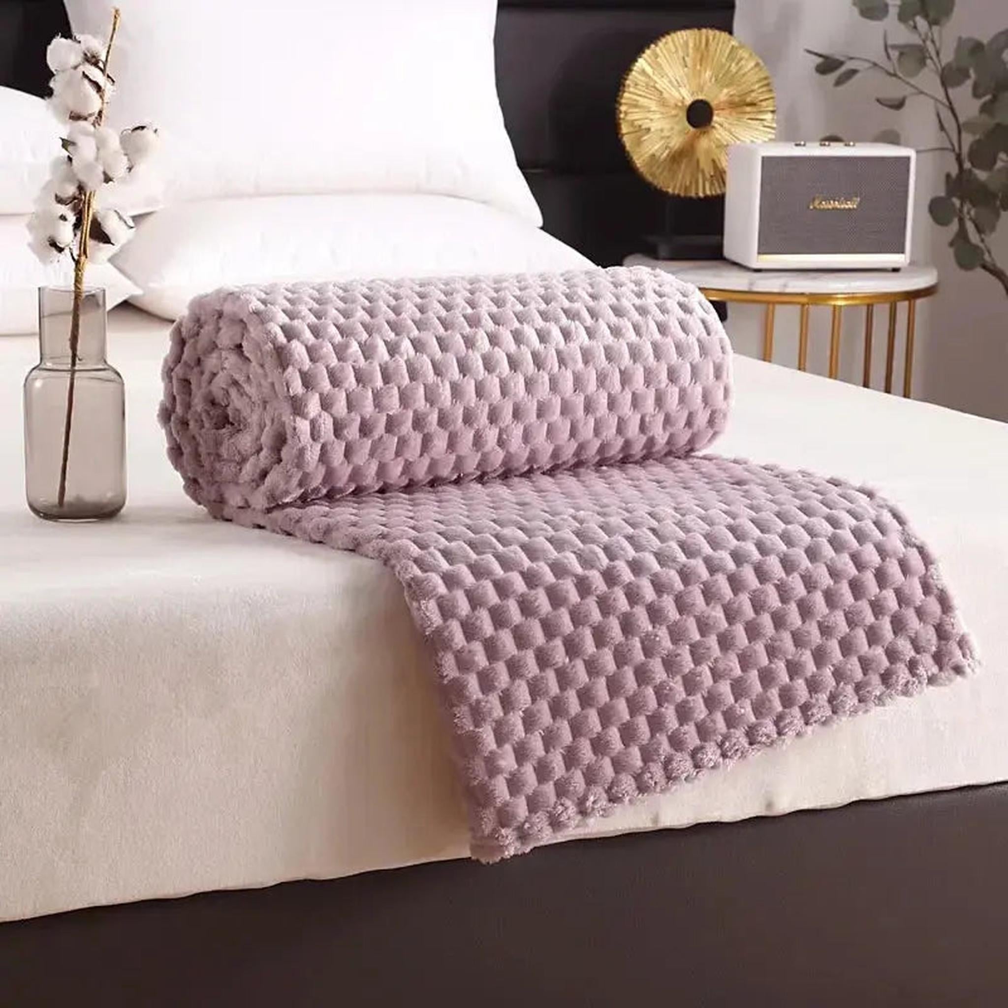Rolled lavender silky flannel fleece blanket with a 3D cloud jacquard pattern on a white bed.