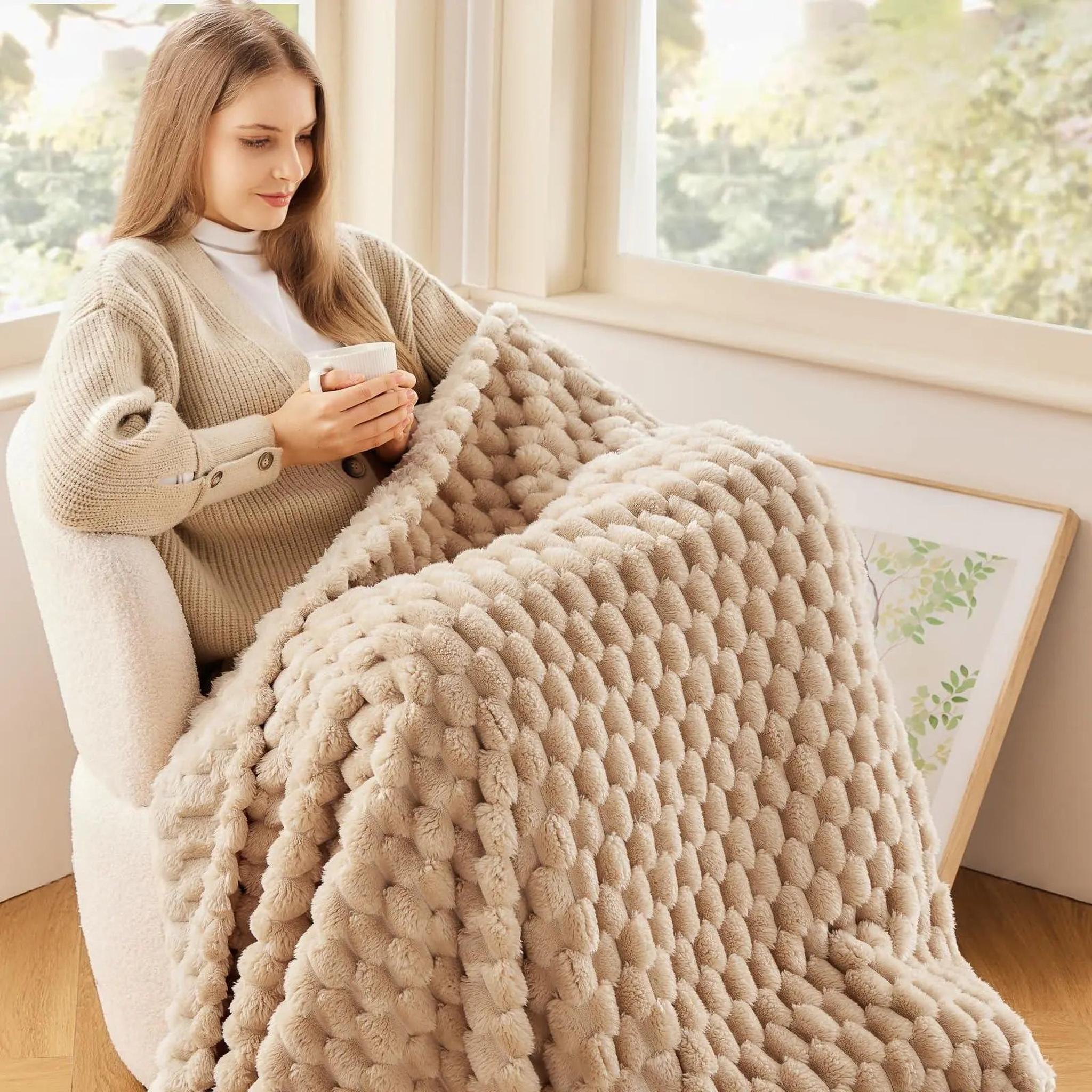 Woman relaxing in a chair, wrapped in a soft beige Clouds Jacquard Fleece Blanket with a 3D cloud pattern.