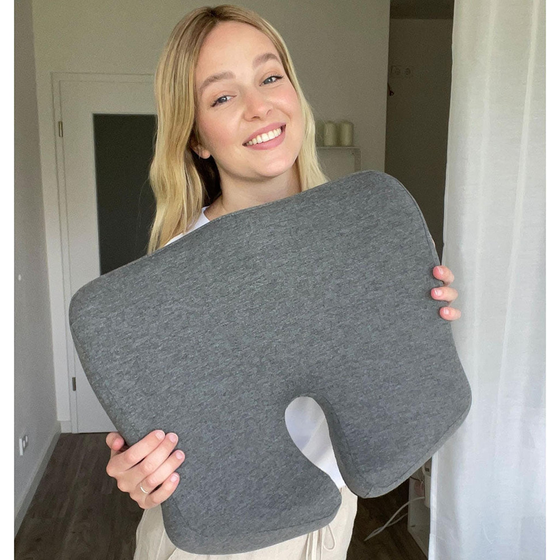 Smiling woman holding a dark gray ergonomic seat cushion with a U-shaped cutout.