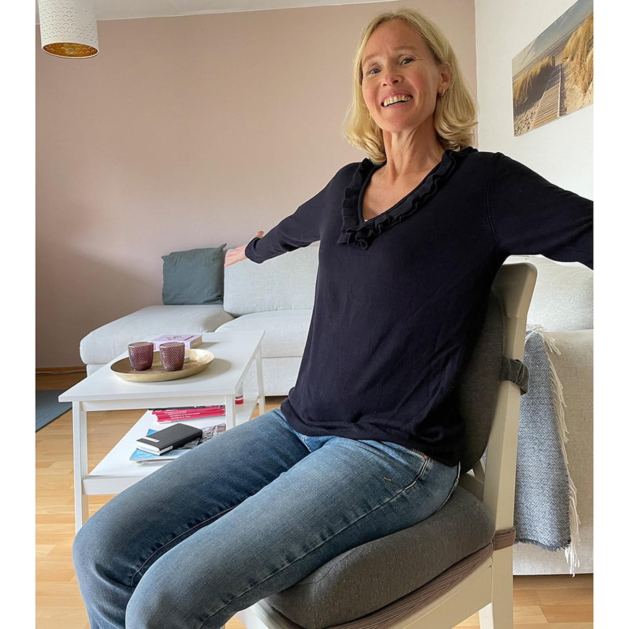 Smiling woman sitting on a gray ergonomic seat and back cushion set on a white chair.