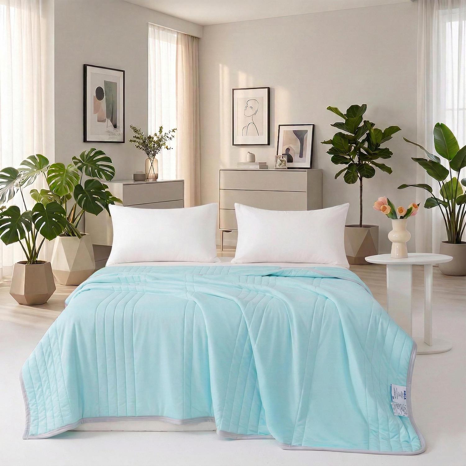Light blue Cool Silk Summer Quilt with subtle quilting, draped over a bed with white pillows in a bright room.