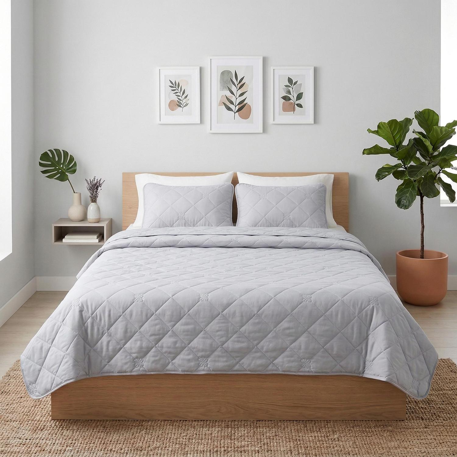 Light gray quilted cooling blanket and two matching pillow shams on a wooden bed.