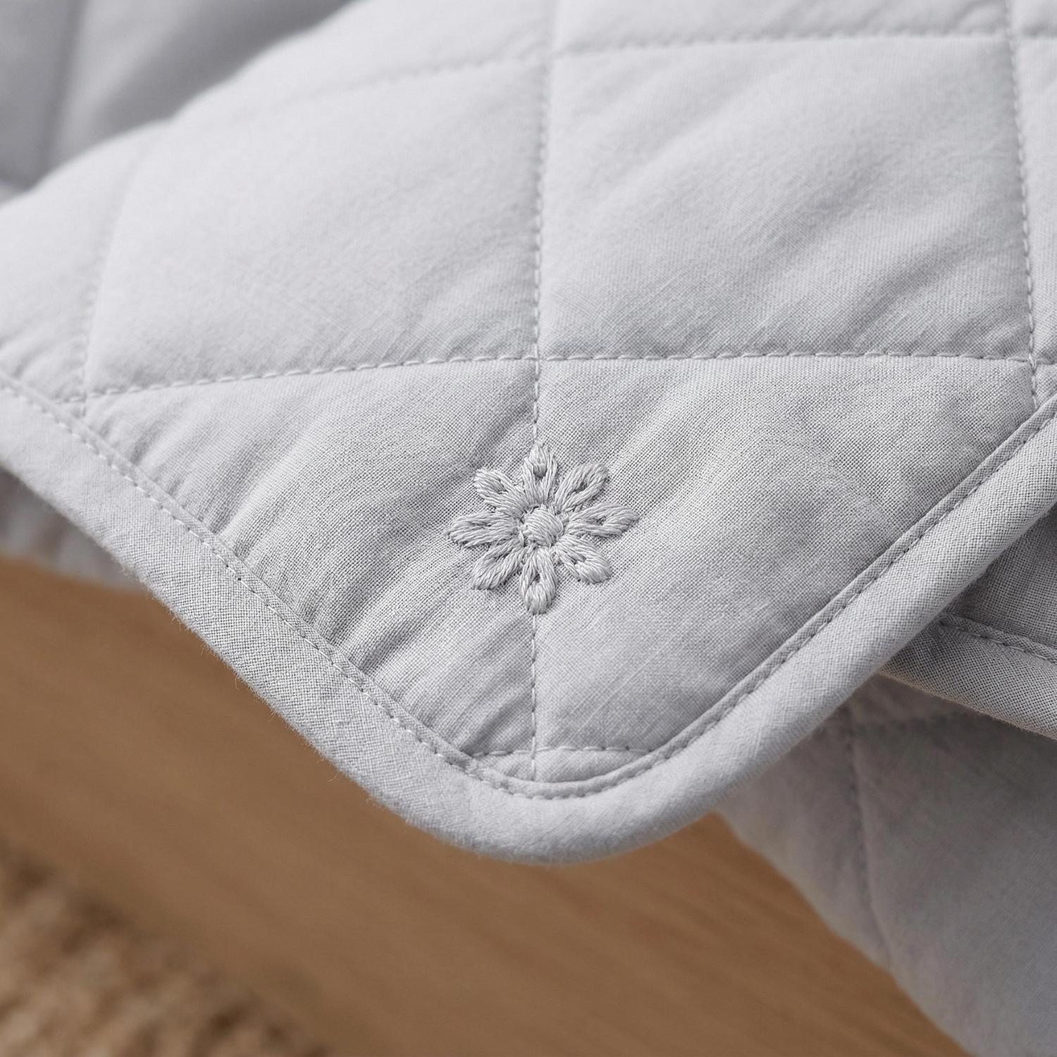 Light gray cooling blanket with subtle quilted pattern and embroidered floral detail.