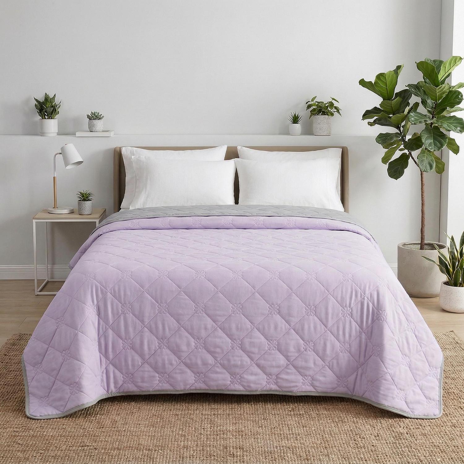 Light purple and grey reversible cooling quilt blanket with diamond quilting and floral patterns on a bed.