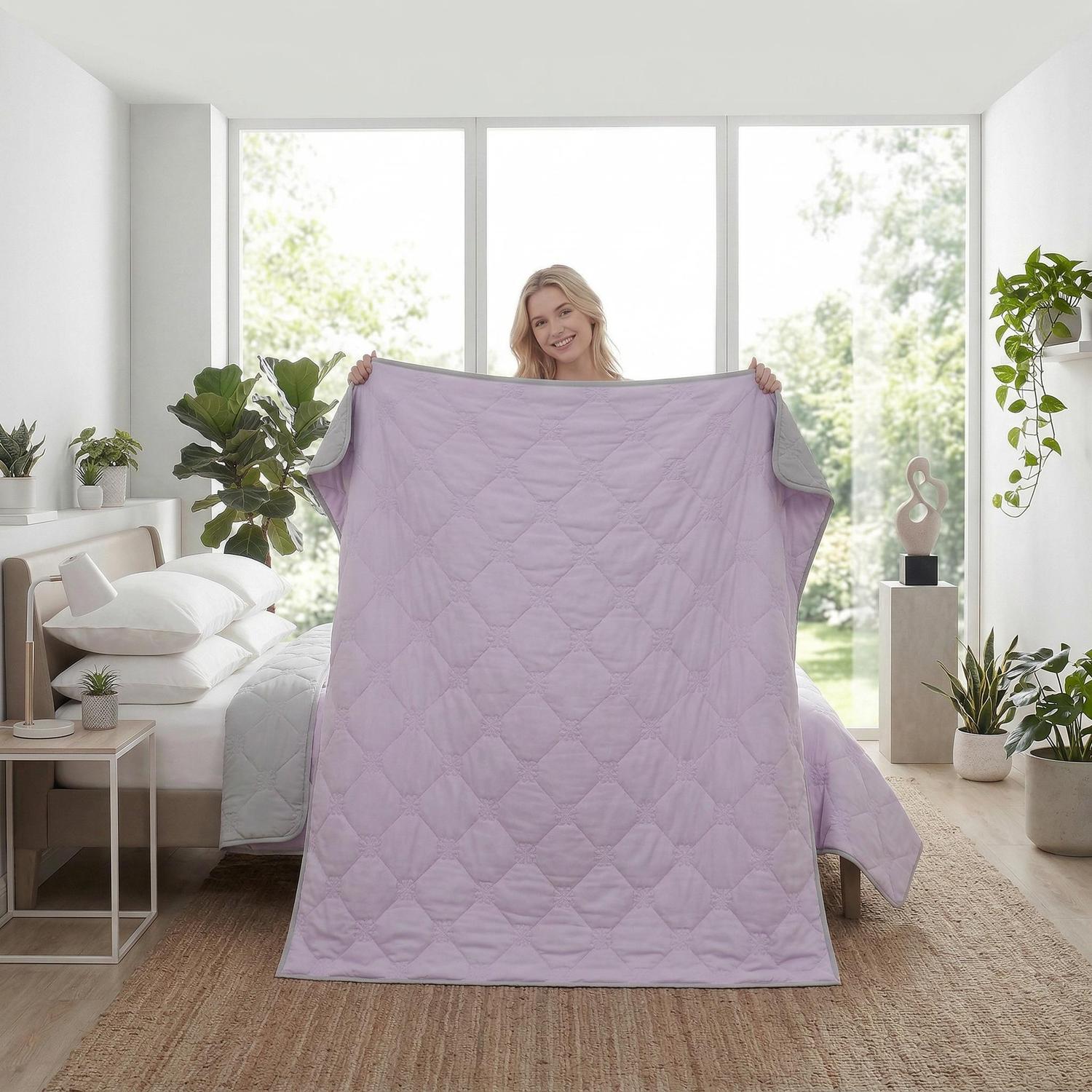 Smiling woman holding up a lavender and gray dual-color cooling blanket with diamond quilting.