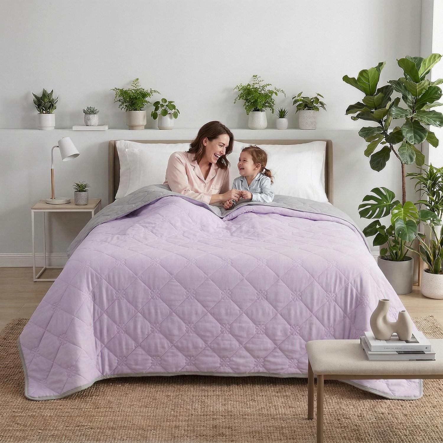 Lavender and gray cooling blanket on a bed with a mother and child, surrounded by plants.
