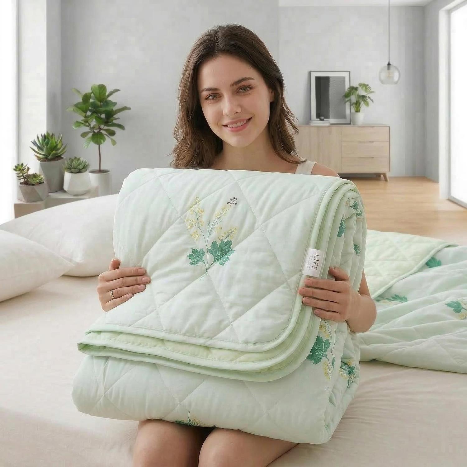 Woman holding a folded light green cooling blanket with quilted diamond stitching and yellow floral embroidery.