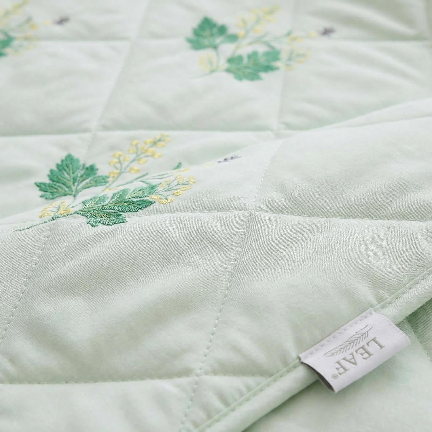 Light green quilted cooling blanket with embroidered yellow and green leaf patterns, featuring a "LEAF" brand tag.