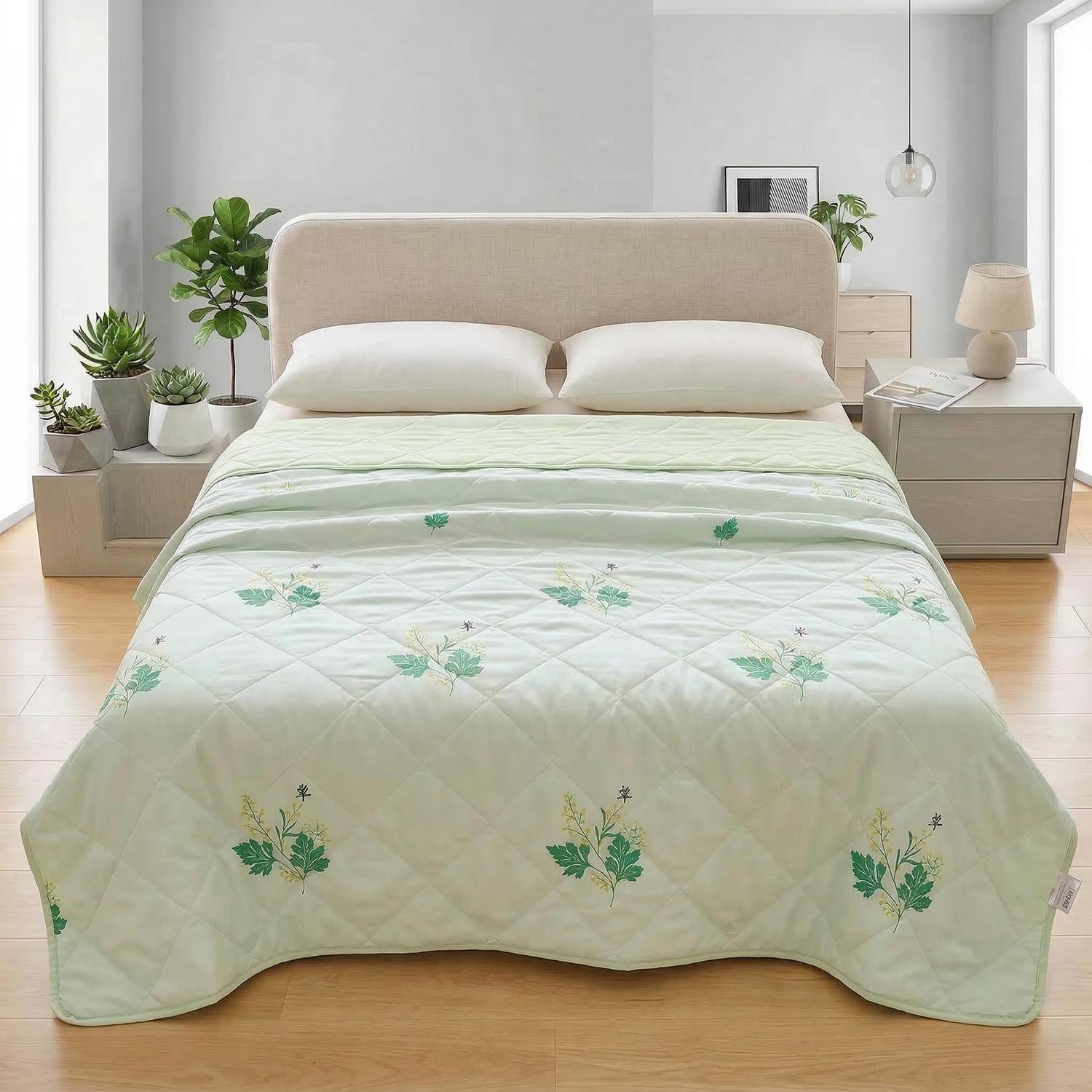 Light green polyester cooling blanket with quilted diamond pattern and green leaf embroidery on a bed.