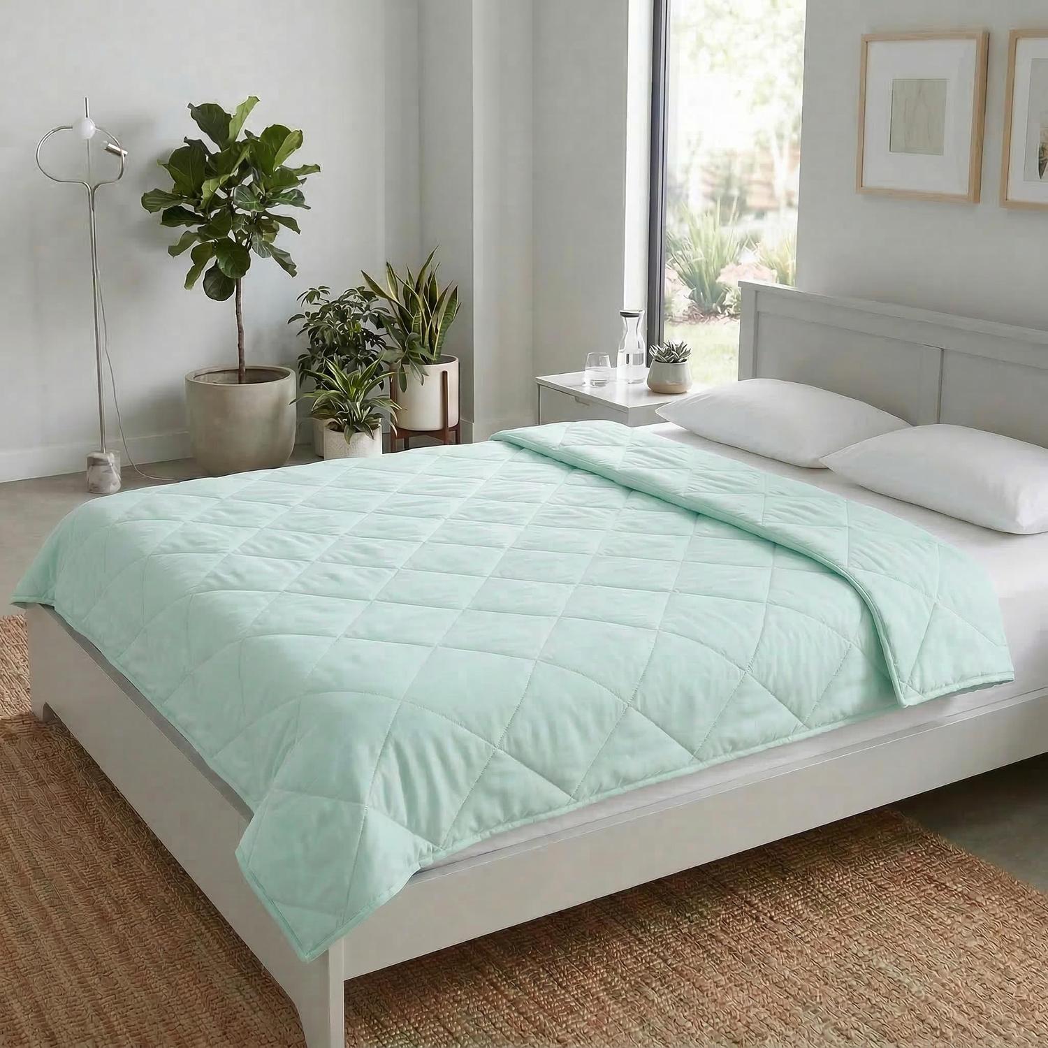 Light green quilted cooling blanket on a white bed, ideal for warm weather comfort.