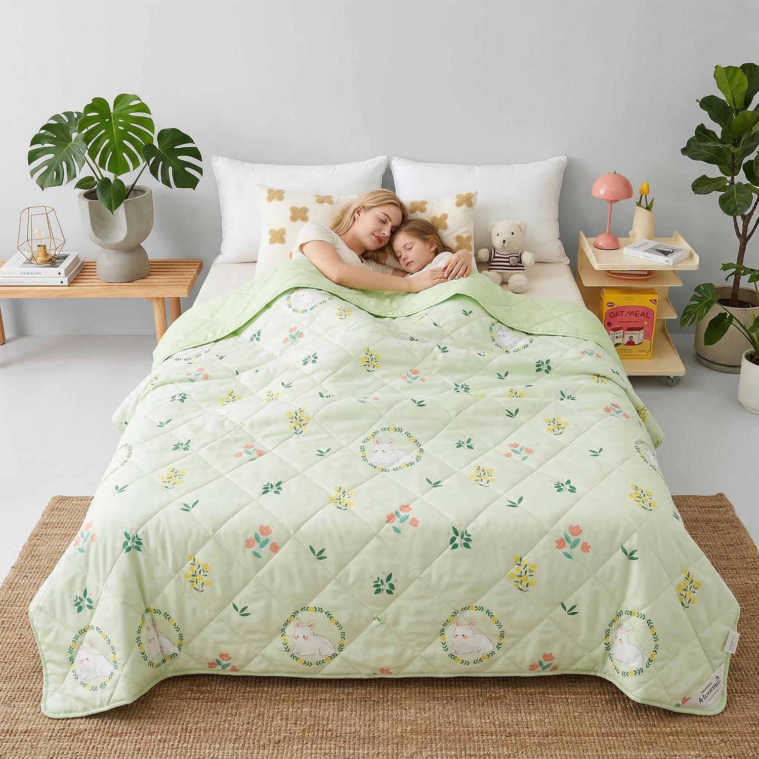 Mother and child sleeping under a light green quilted cooling blanket with bunny and floral patterns.