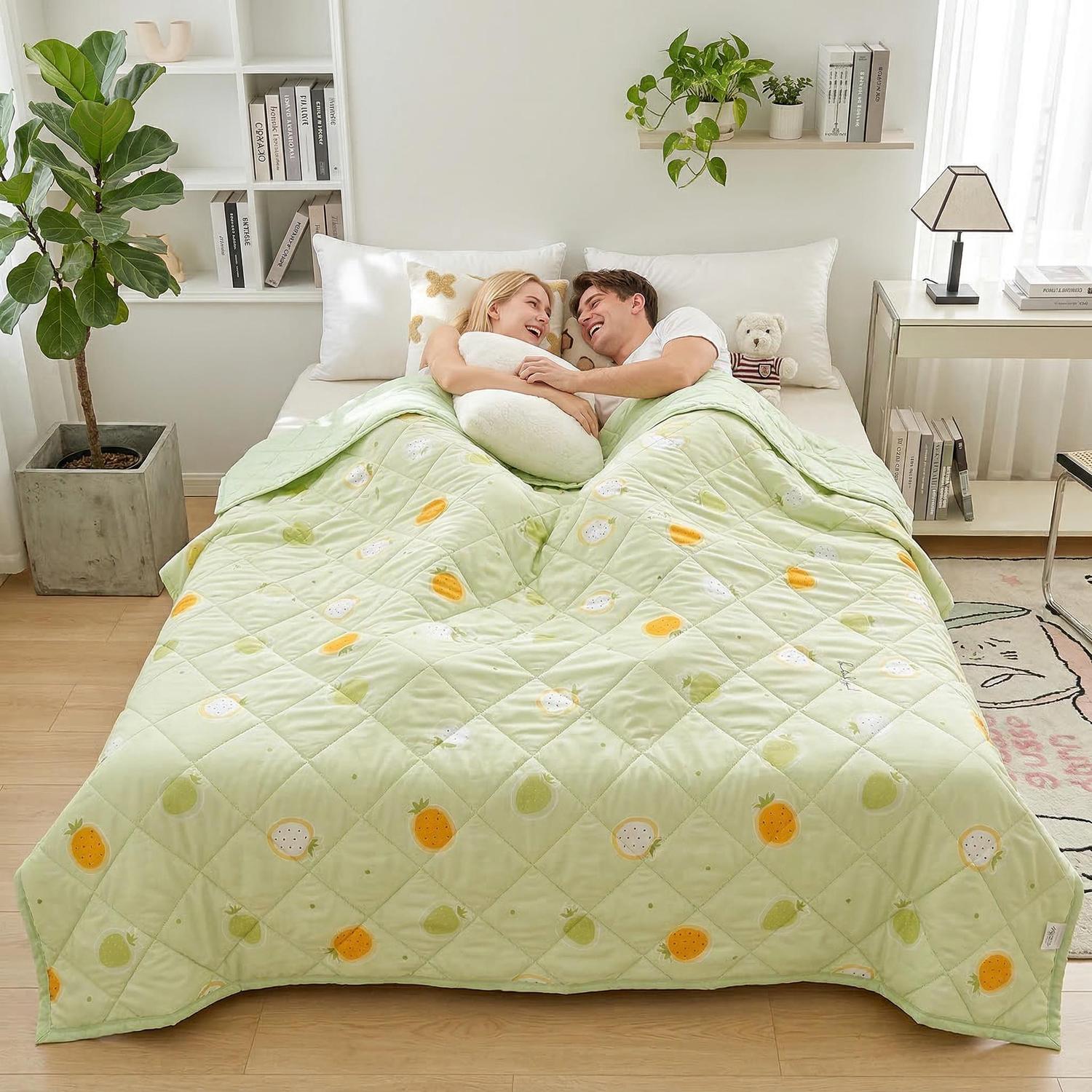 Couple laughing in bed under a light green quilted cooling blanket with fruit patterns.