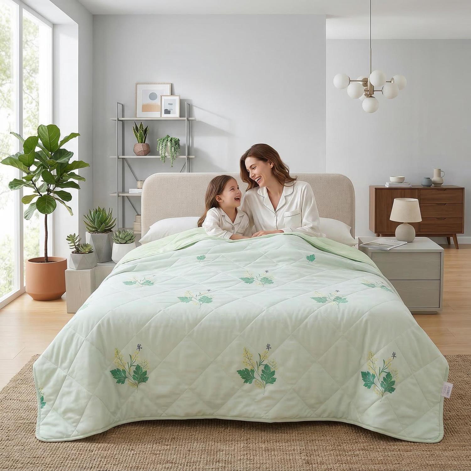 Mother and child under a light green quilted cooling blanket with subtle leaf embroidery.